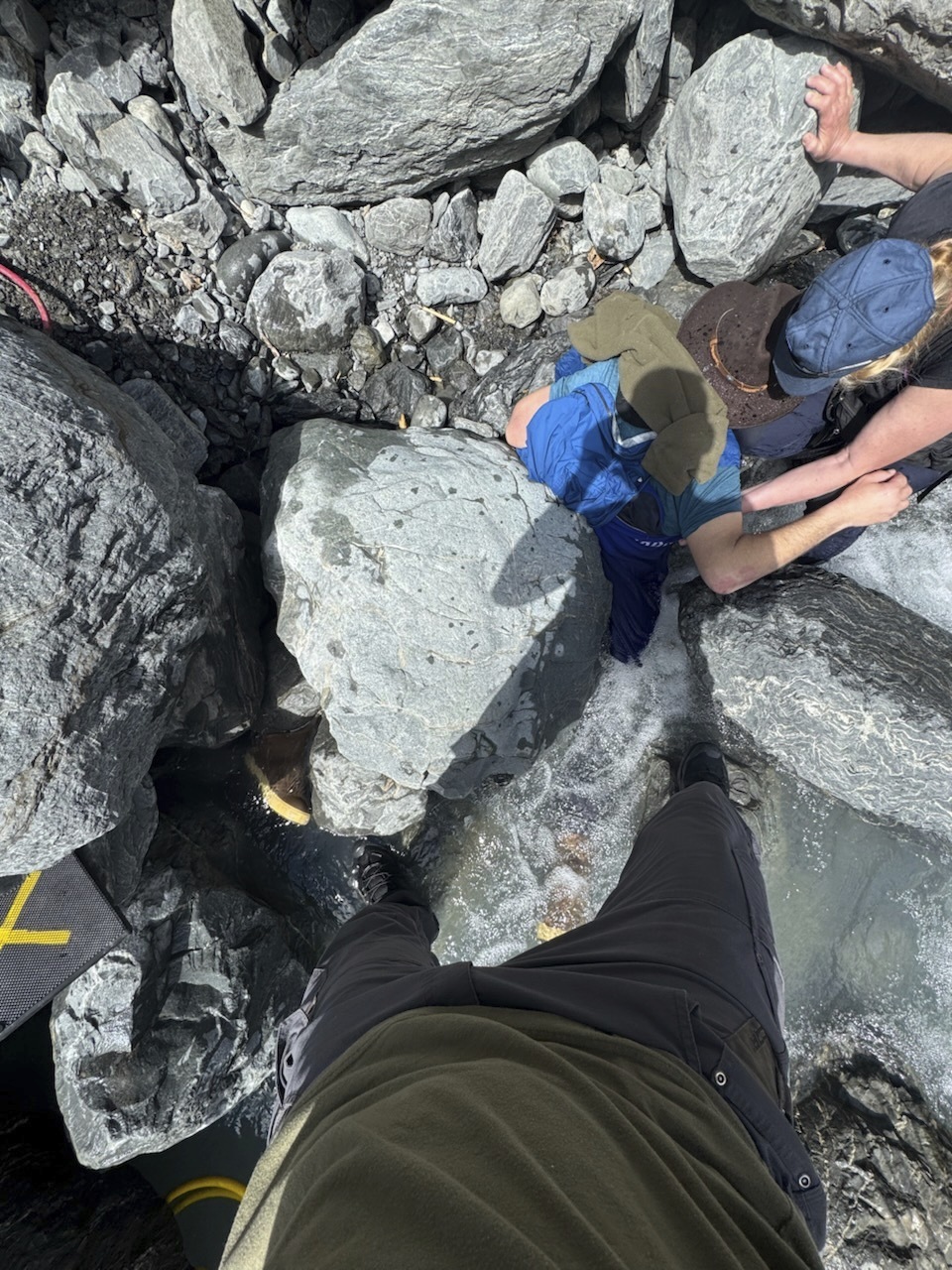 This May 24, 2025, photo shows Kell Morris, upper right in a brown hat, trapped under a 700 pound rock near Seward, Alaska. (Jason Harrington/Seward Fire Department via AP)