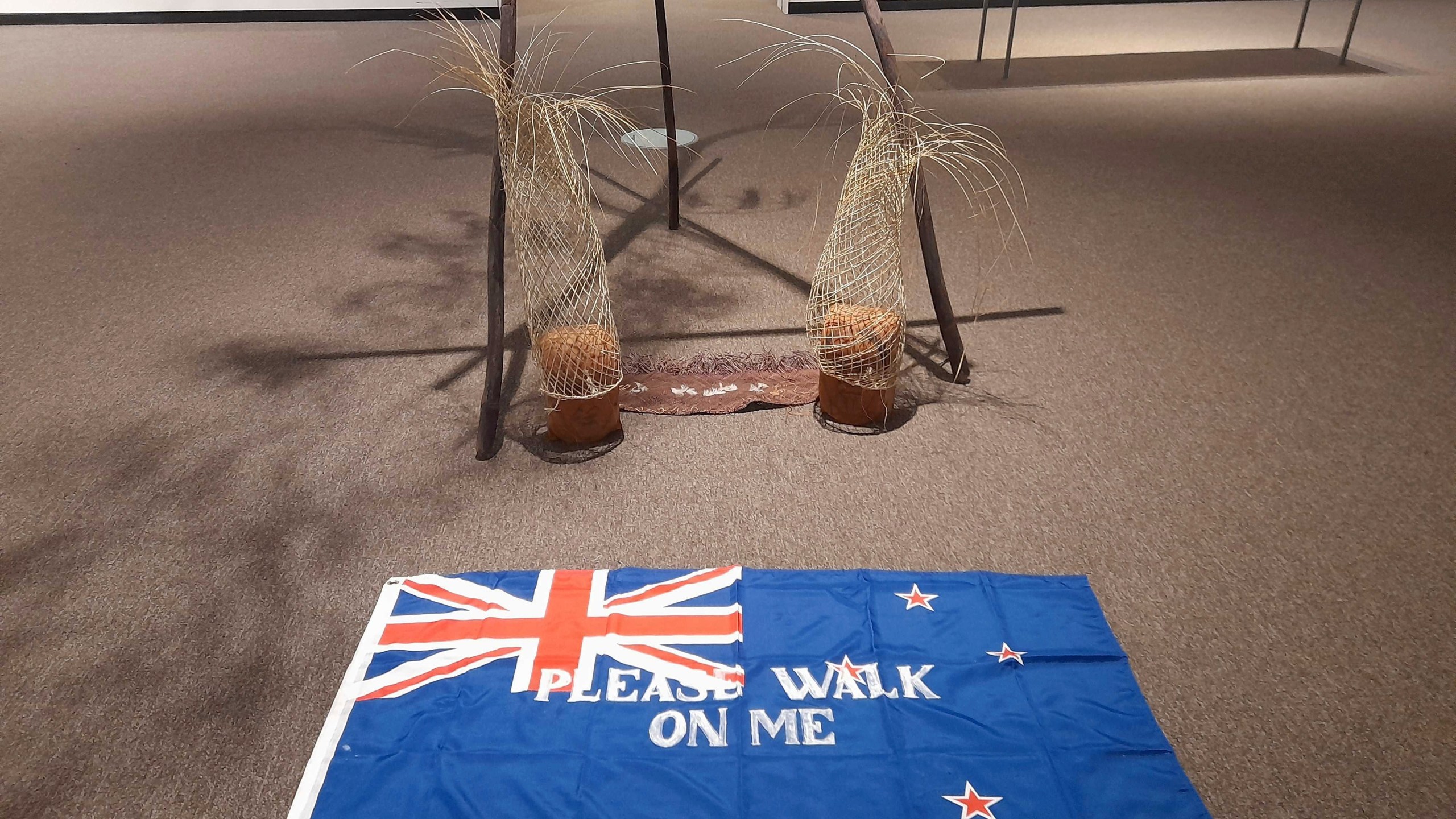 An artwork titled Flagging the Future, a cloth New Zealand flag with the words "please walk on me" stenciled across it by Māori artist Diane Prince, is displayed on the floor on Tuesday, May 27, 2025, at the Suter Art Gallery in Nelson, New Zealand. (Catherine Hubbard/Nelson Mail/STUFF via AP)