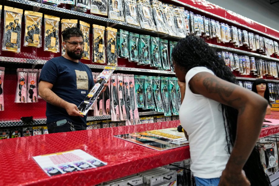An employee at Seven Daughters, a beauty supply store in College Park, Ga., left, assists a customer as she searches for human hair bundles, Tuesday, May 6, 2025. (AP Photo/Stephanie Scarbrough)