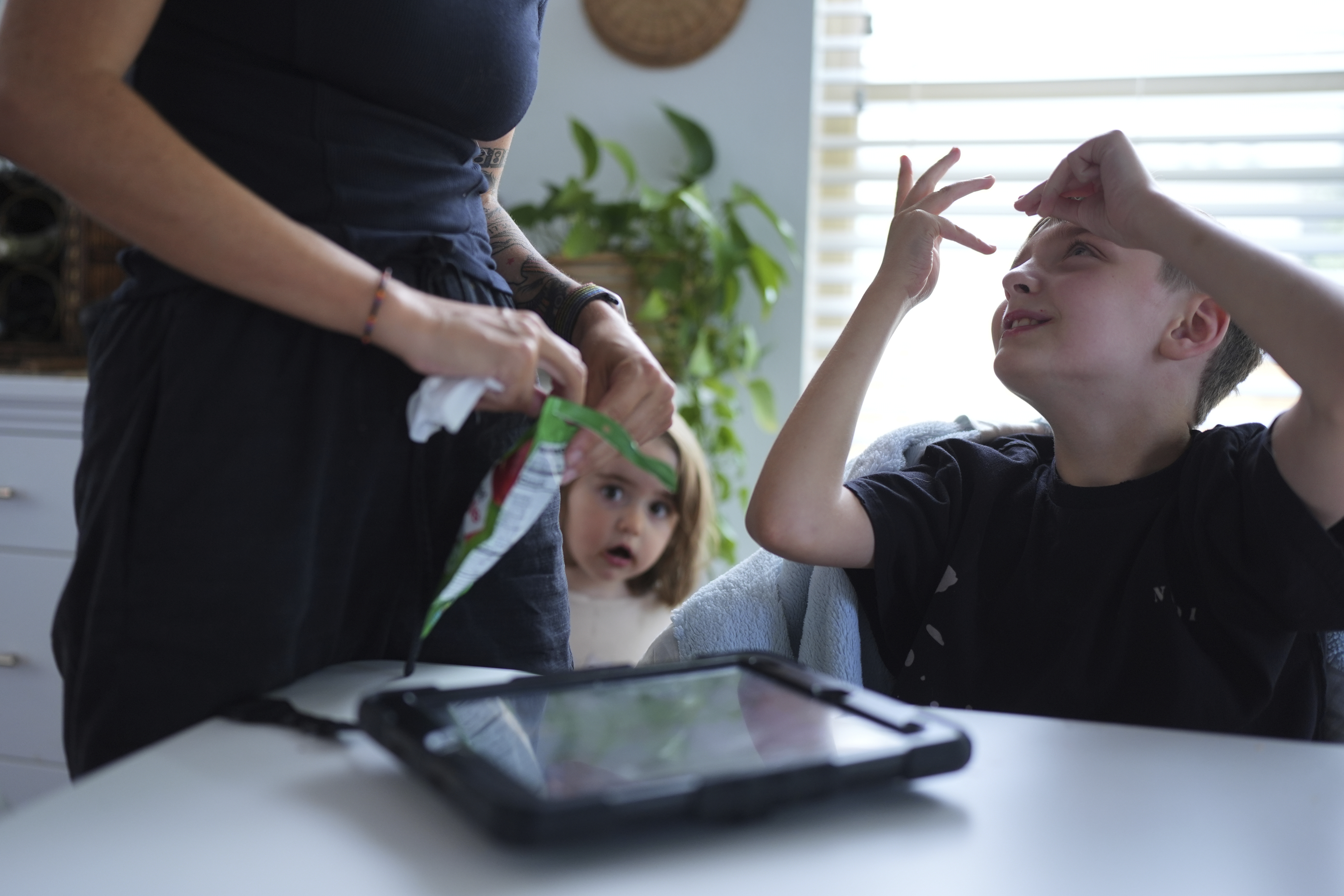 Charlie Lamb, right, who is diagnosed with autism and is non-verbal, uses an AAC device to communicate with his mother Eileen Lamb left, who also has autism, as Charlie's sister Billie looks on, Monday, May 12, 2025, in Austin, Texas. (AP Photo/Eric Gay)