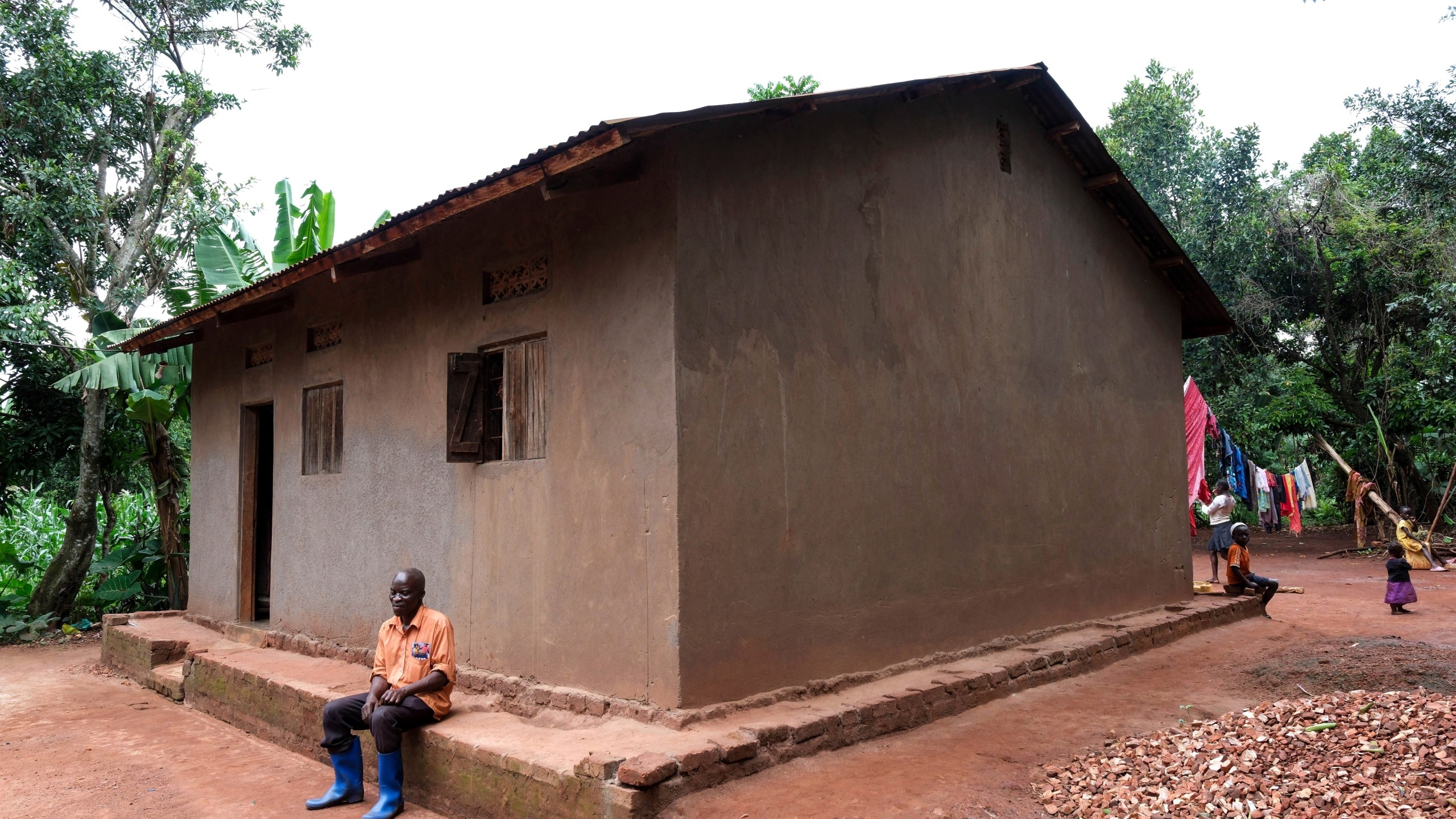 Simon Tigawalana rests in front of his house with clay-based earthen floors by EarthEnable on May 16, 2025, in Jinja, Uganda. (AP Photo/Hajarah Nalwadda)