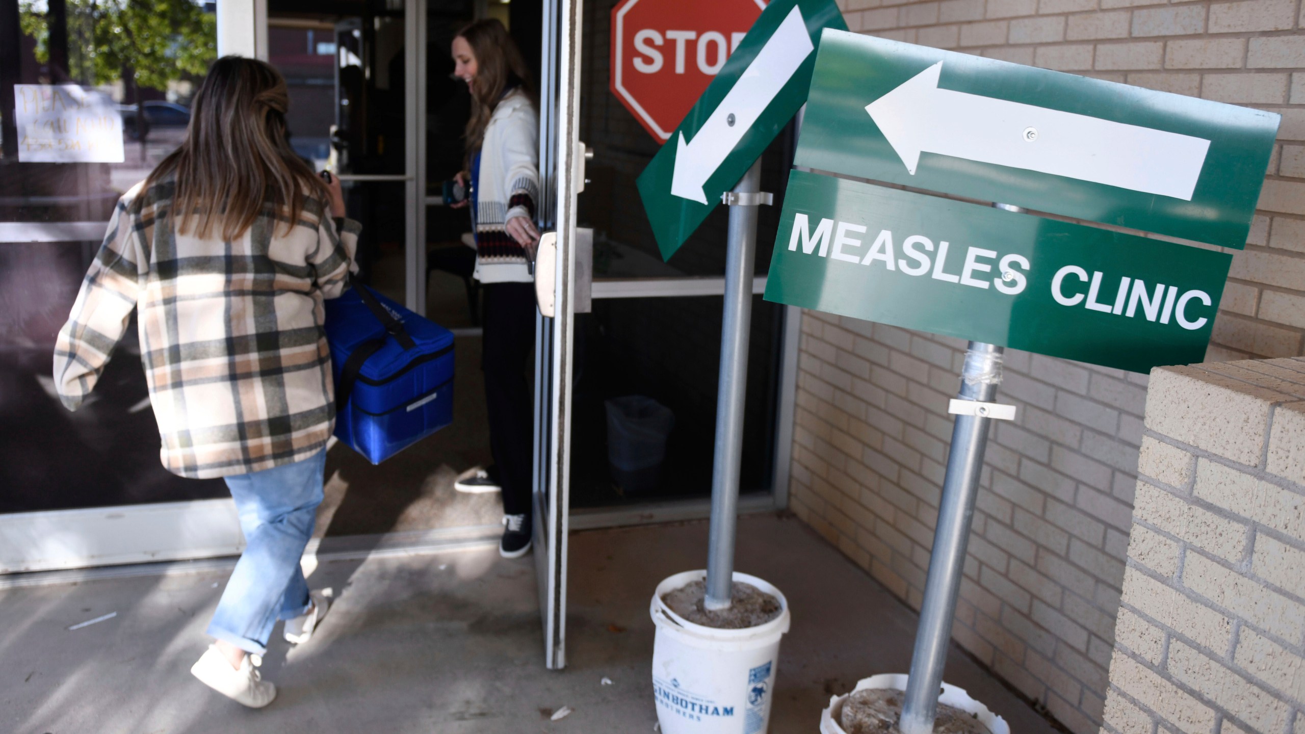 FILE - Health department staff members enter the Andrews County Health Department measles clinic carrying doses of the measles, mumps and rubella vaccine, Tuesday, April 8, 2025, in Andrews, Texas. (AP Photo/Annie Rice, File)