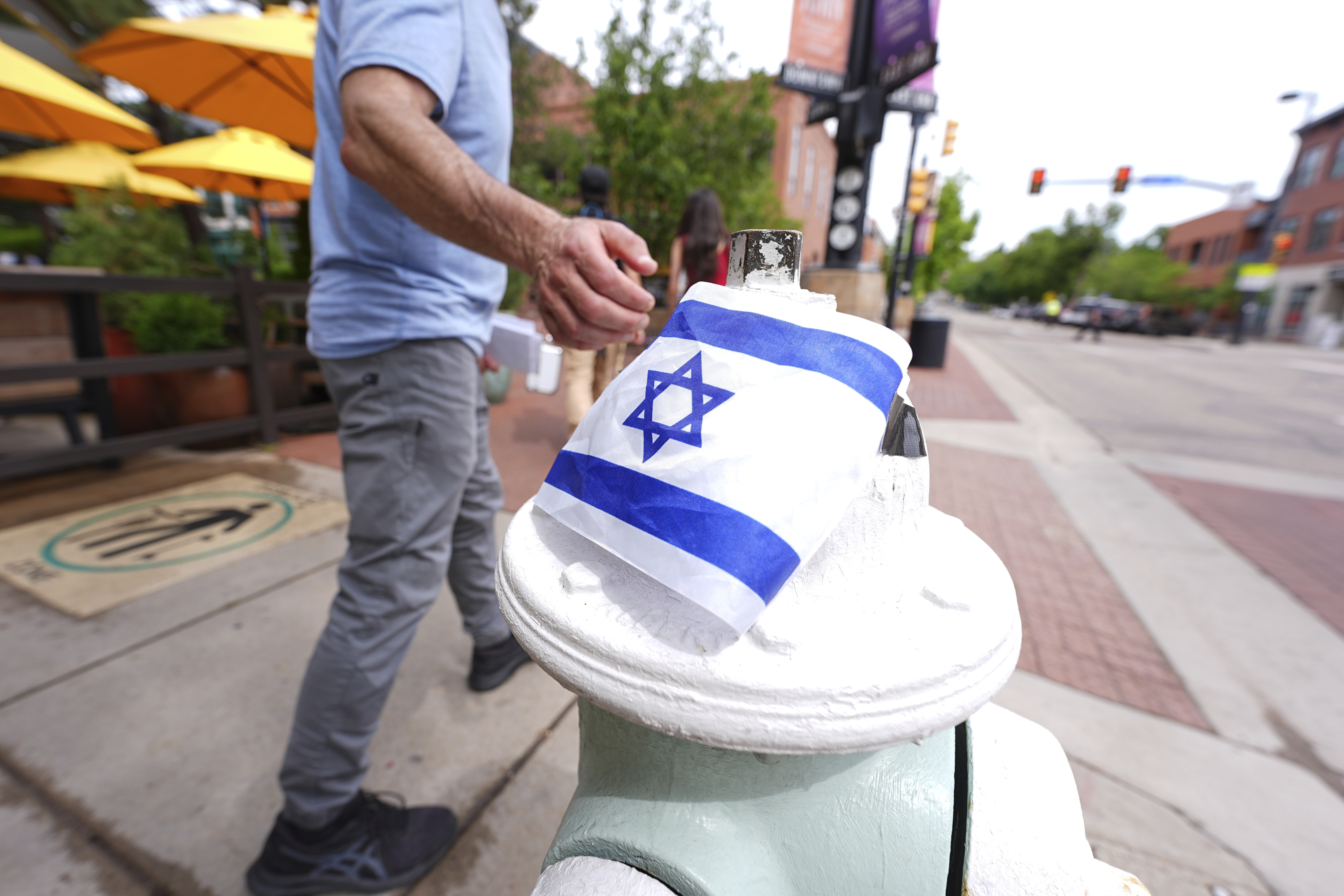 A passer-by touches the flag of Israel taped on to the top of a bollard on the east end of the Pearl Street Mall near the Boulder County, Colo., courthouse Monday, June 2, 2025, in Boulder, Colo. (AP Photo/David Zalubowski)
