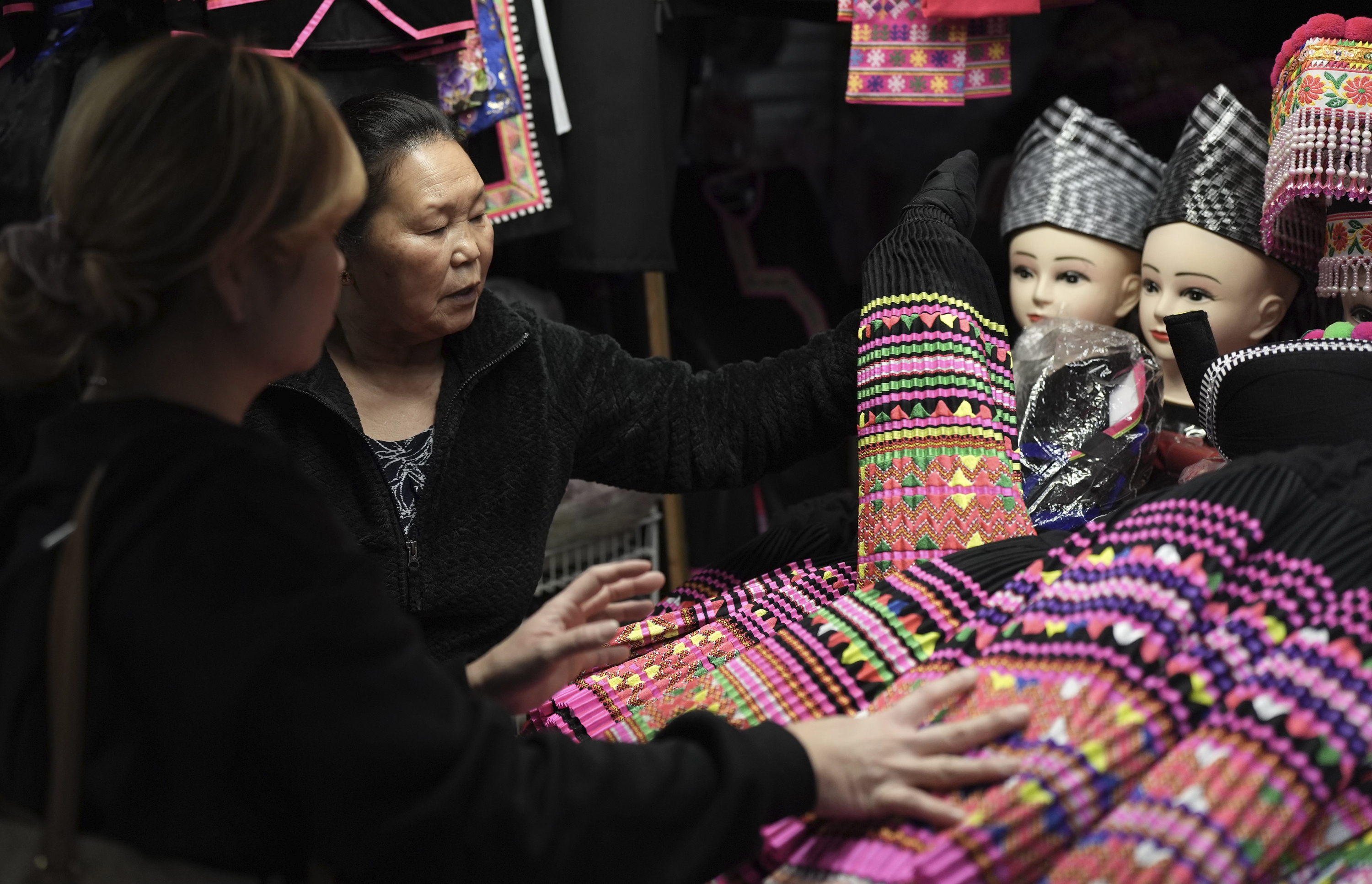 FILE - Shoppers look for pleated skirts and other clothing for Hmong New Year for sale at the stall of Elisa Her, left, in the Hmong Village covered market in St. Paul, Minn., on Thursday, Nov. 16, 2023. (AP Photo/Mark Vancleave, file)