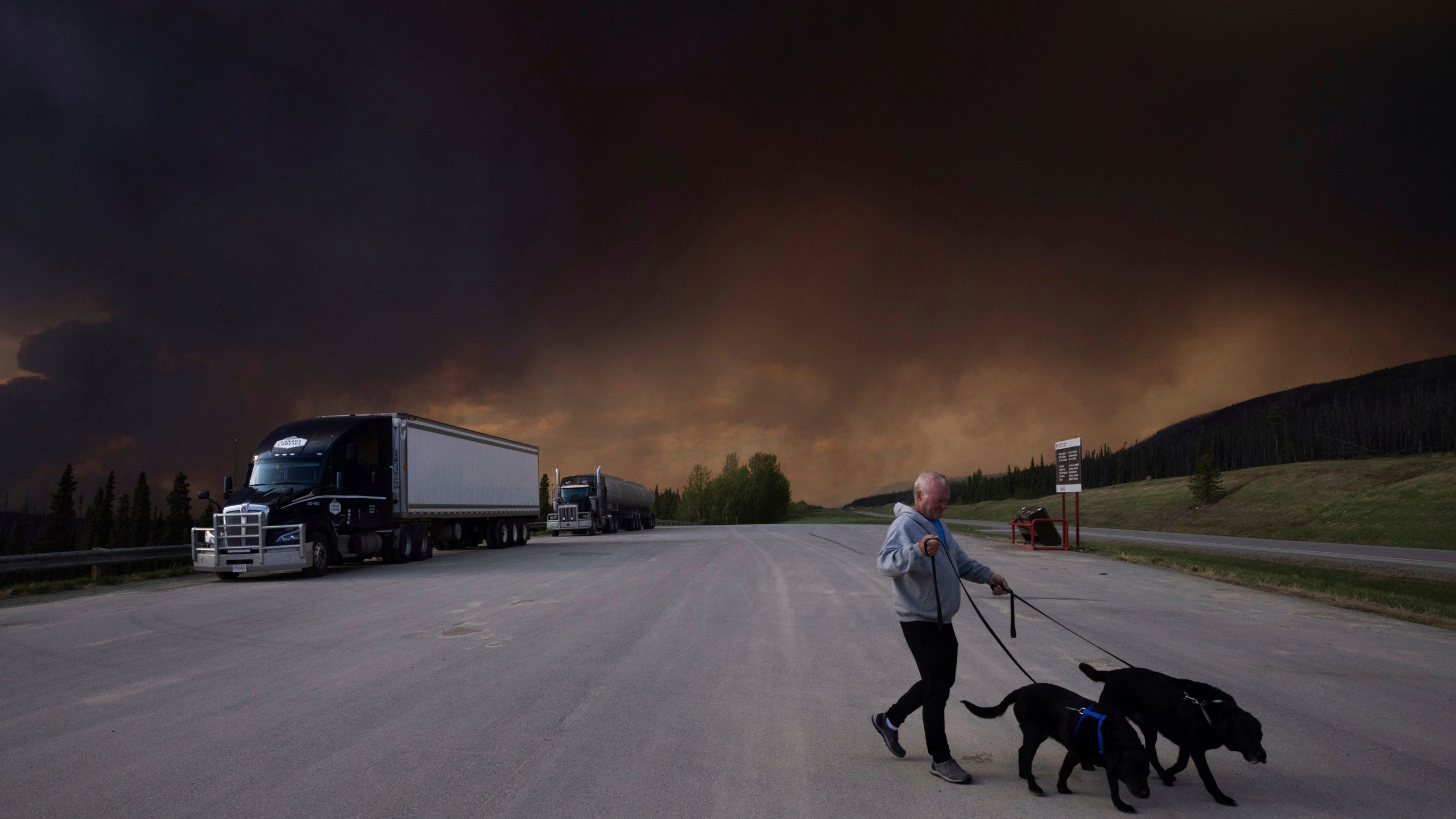FILE - A person takes his dogs out for a quick break under billowing wildfire smoke off Highway 97 north of Buckinghorse River, British Columbia, May 30, 2025. (Nasuna Stuart-Ulin/The Canadian Press via AP, File)