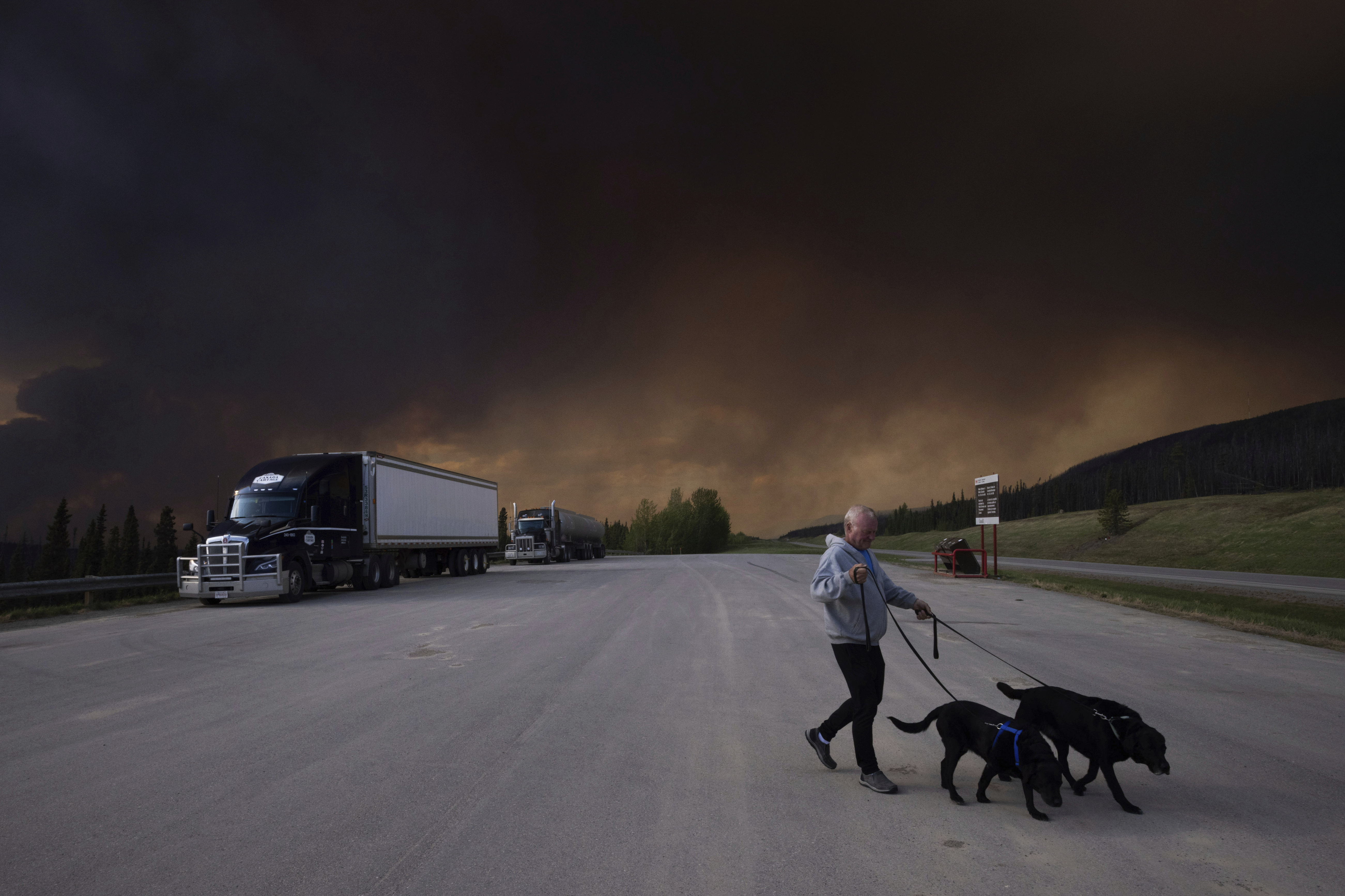 FILE - A person takes his dogs out for a quick break under billowing wildfire smoke off Highway 97 north of Buckinghorse River, British Columbia, May 30, 2025. (Nasuna Stuart-Ulin/The Canadian Press via AP, File)