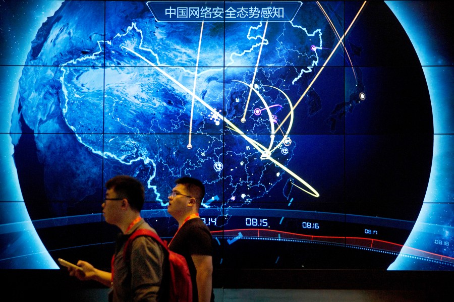 FILE - Attendees walk past an electronic display showing recent cyberattacks in China at the China Internet Security Conference in Beijing, on Sept. 12, 2017. (AP Photo/Mark Schiefelbein, File)