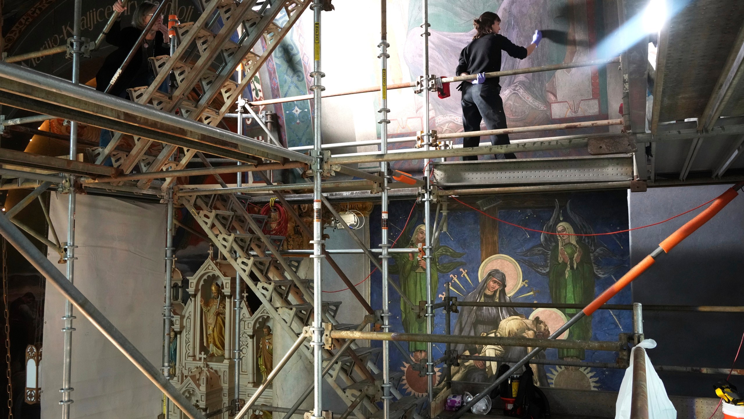 Working on a 32-foot-tall scaffold, art conservator Kate Pirelli works on cleaning a mural by Max Vanka inside St. Nicholas Croatian Catholic Church in Millvale, Pa., Monday, May 19, 2025. (AP Photo/Gene J. Puskar)