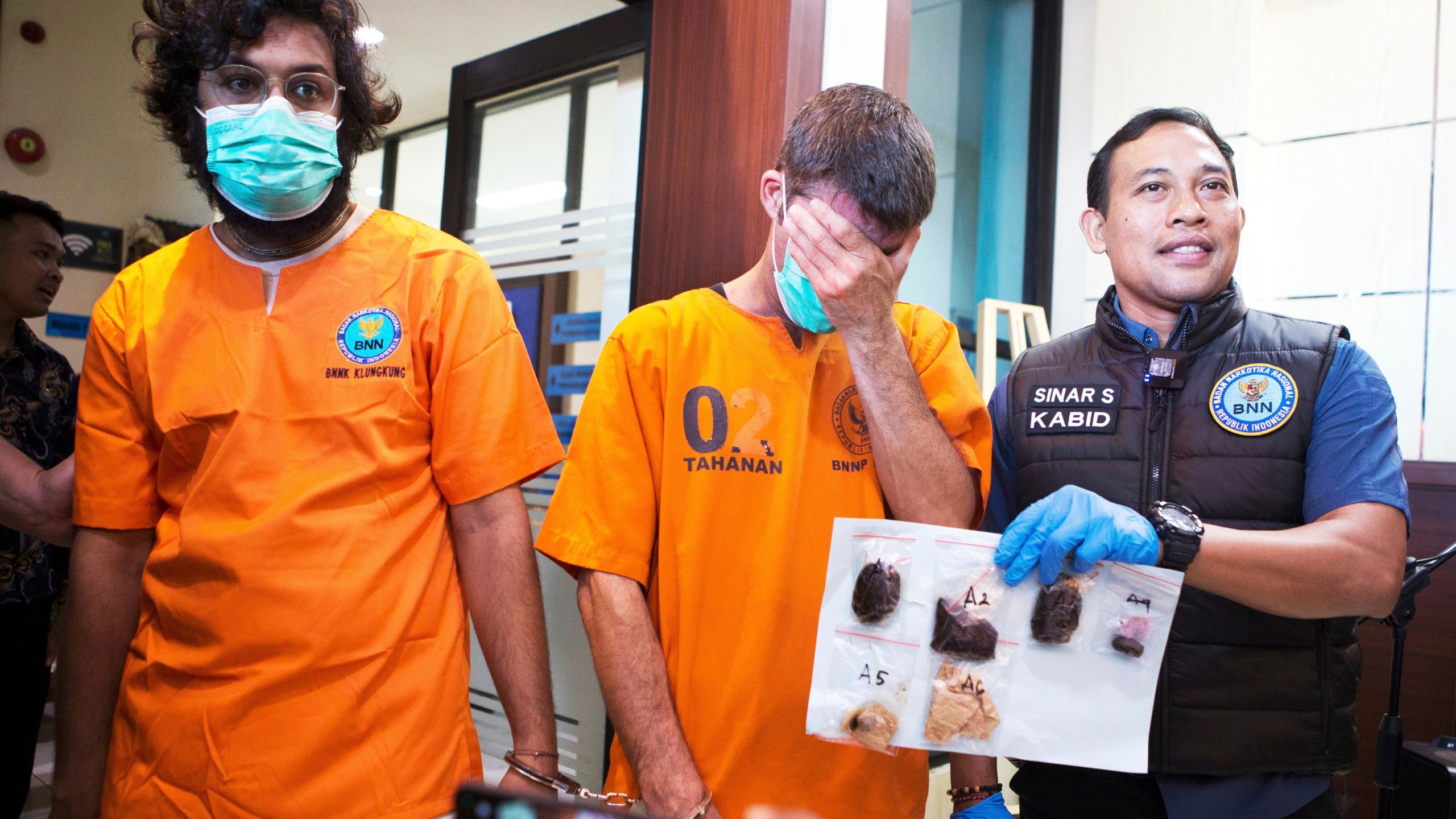 Australian national identified only as P.R., center, and an Indian national identified as H.V., left, who were arrested for drug possession, react as a National Narcotics Agency officer shows evidence confiscated from them, during a press conference in Denpasar, Bali, Indonesia Thursday, June 5, 2025. (AP Photo/Firdia Lisnawati)