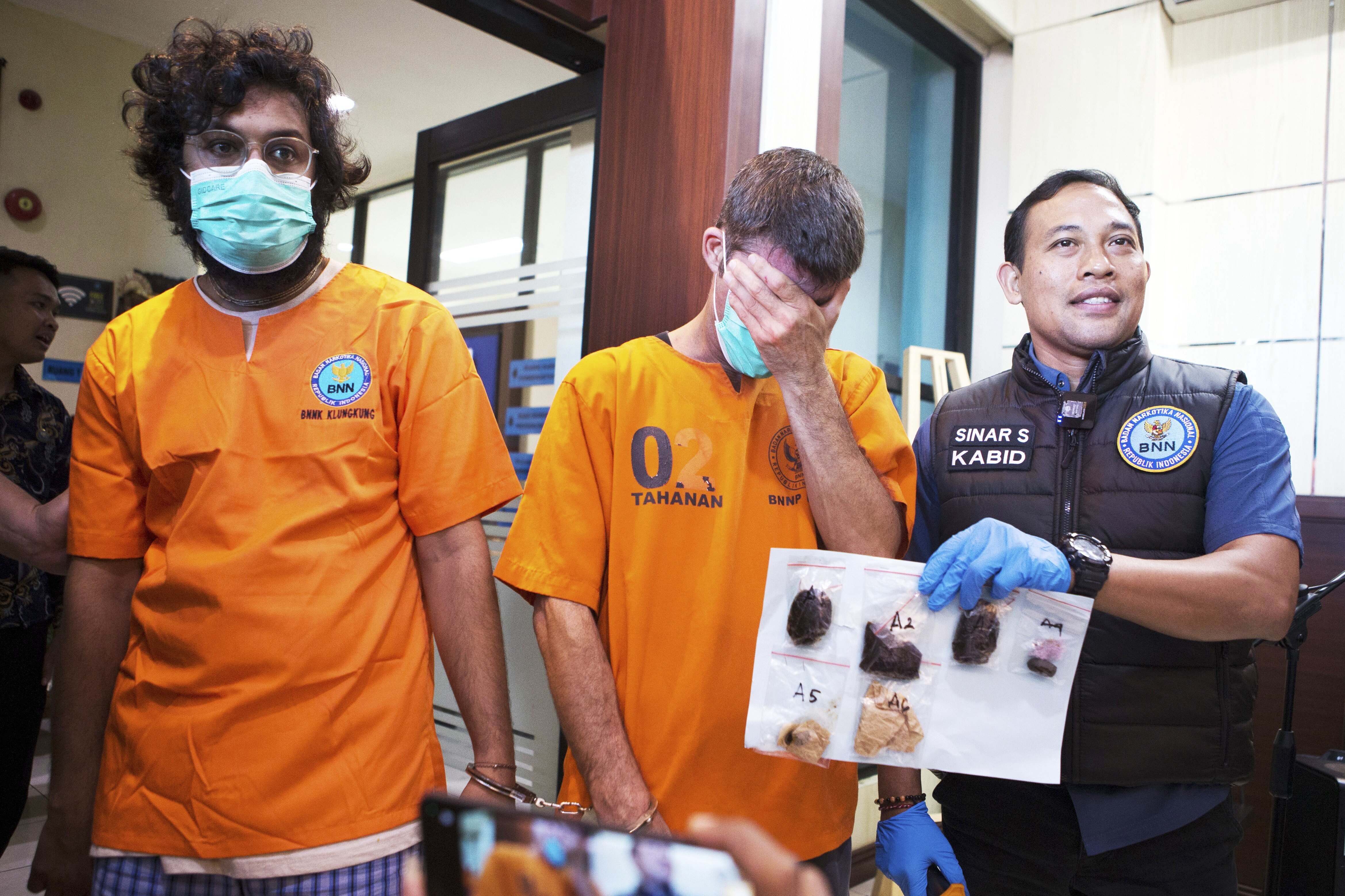 Australian national identified only as P.R., center, and an Indian national identified as H.V., left, who were arrested for drug possession, react as a National Narcotics Agency officer shows evidence confiscated from them, during a press conference in Denpasar, Bali, Indonesia Thursday, June 5, 2025. (AP Photo/Firdia Lisnawati)