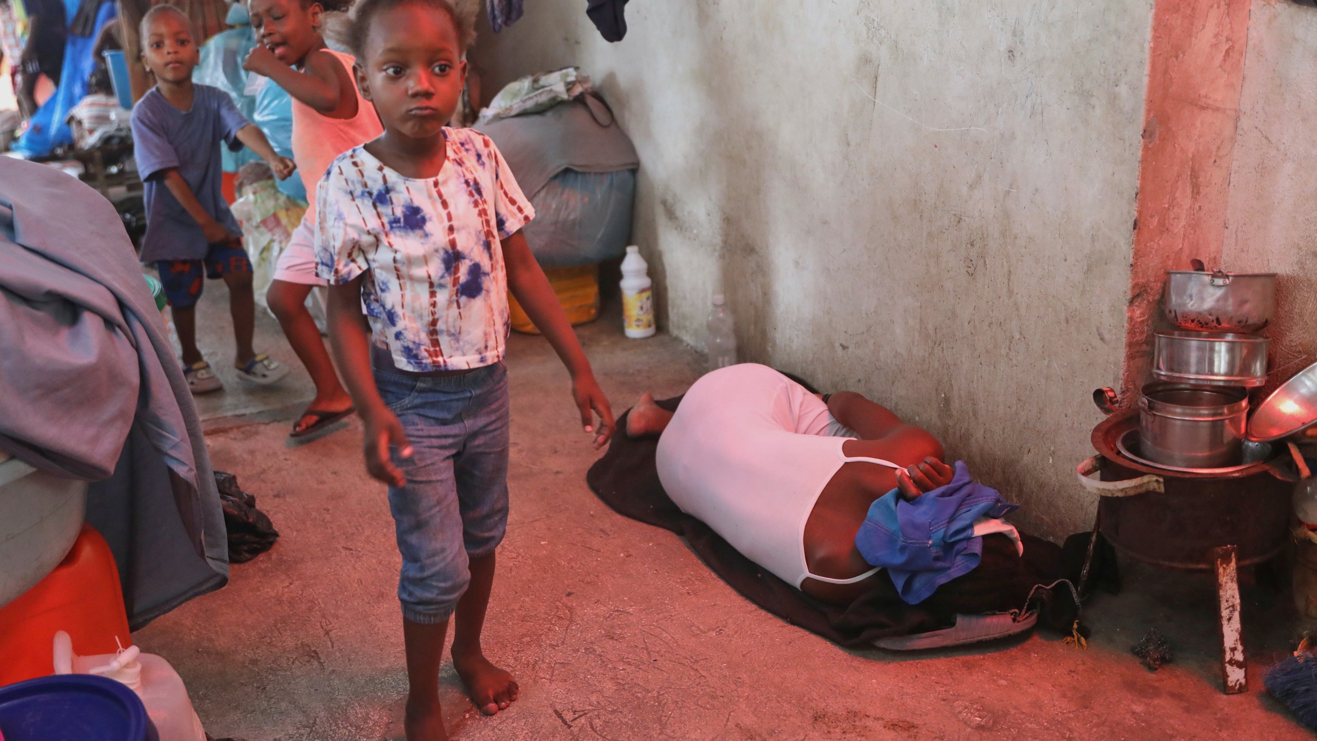 A woman sleeps on a blanket next to children playing in a hallway at a shelter for families displaced by gang violence in Port-au-Prince, Haiti, Monday, May 12, 2025. (AP Photo/Odelyn Joseph)