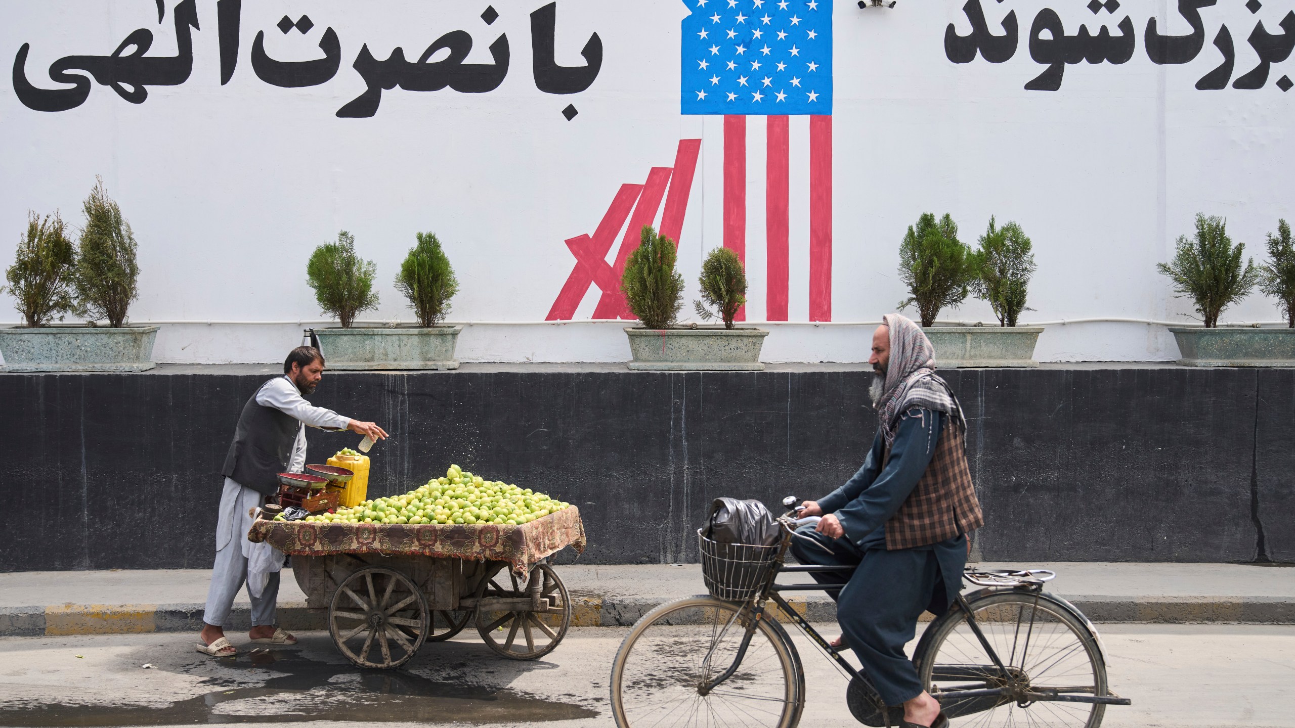 A cyclist passes in front of the former US embassy while a vendor waits for customers, in Kabul, Afghanistan, Thursday, June 5, 2025. (AP Photo/Ebrahim Noroozi)