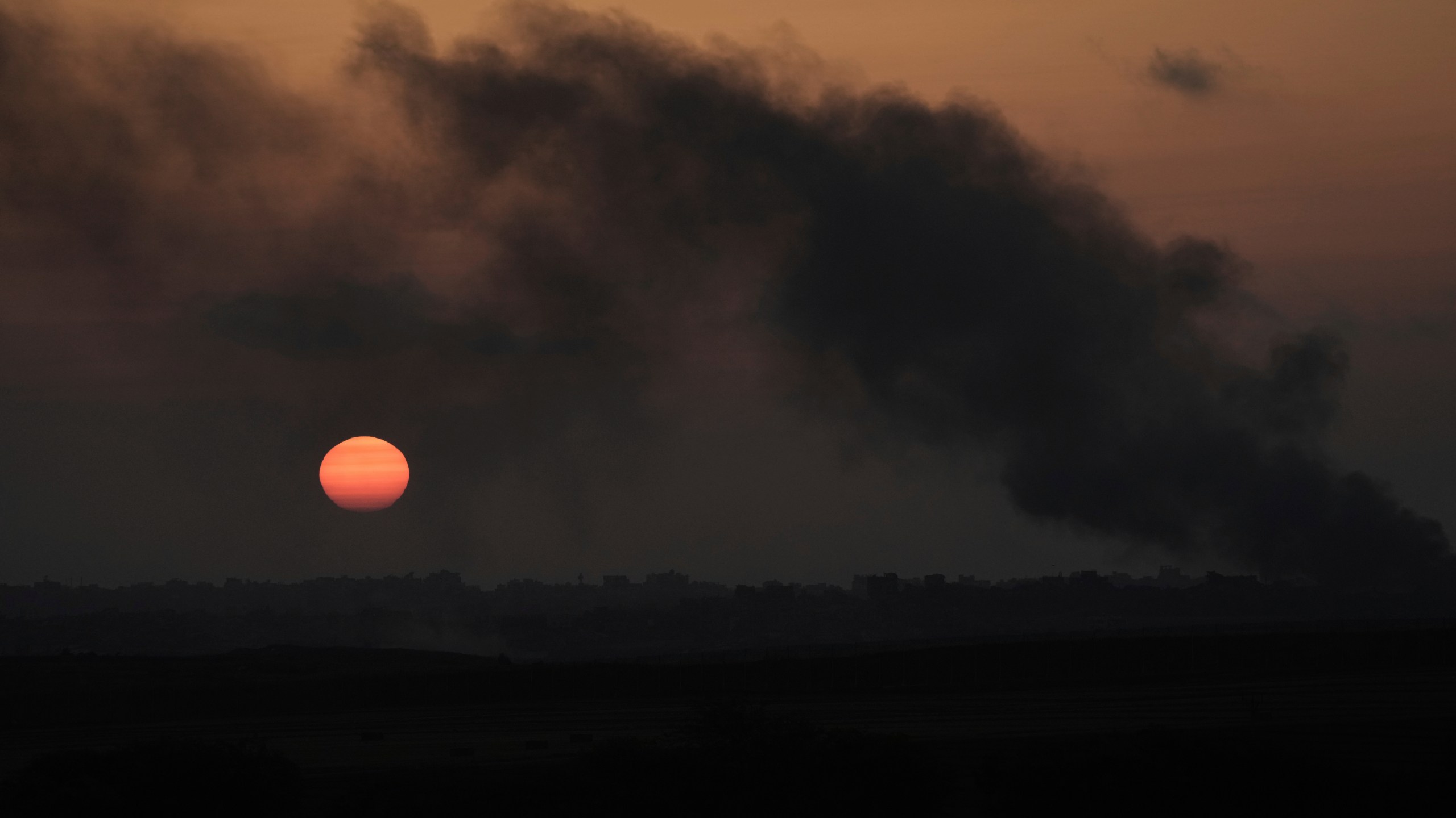 The sun sets as smoke from Israeli bombardment billows over buildings in the northern Gaza Strip, seen from southern Israel, Thursday, June 5, 2025. (AP Photo/Maya Alleruzzo)