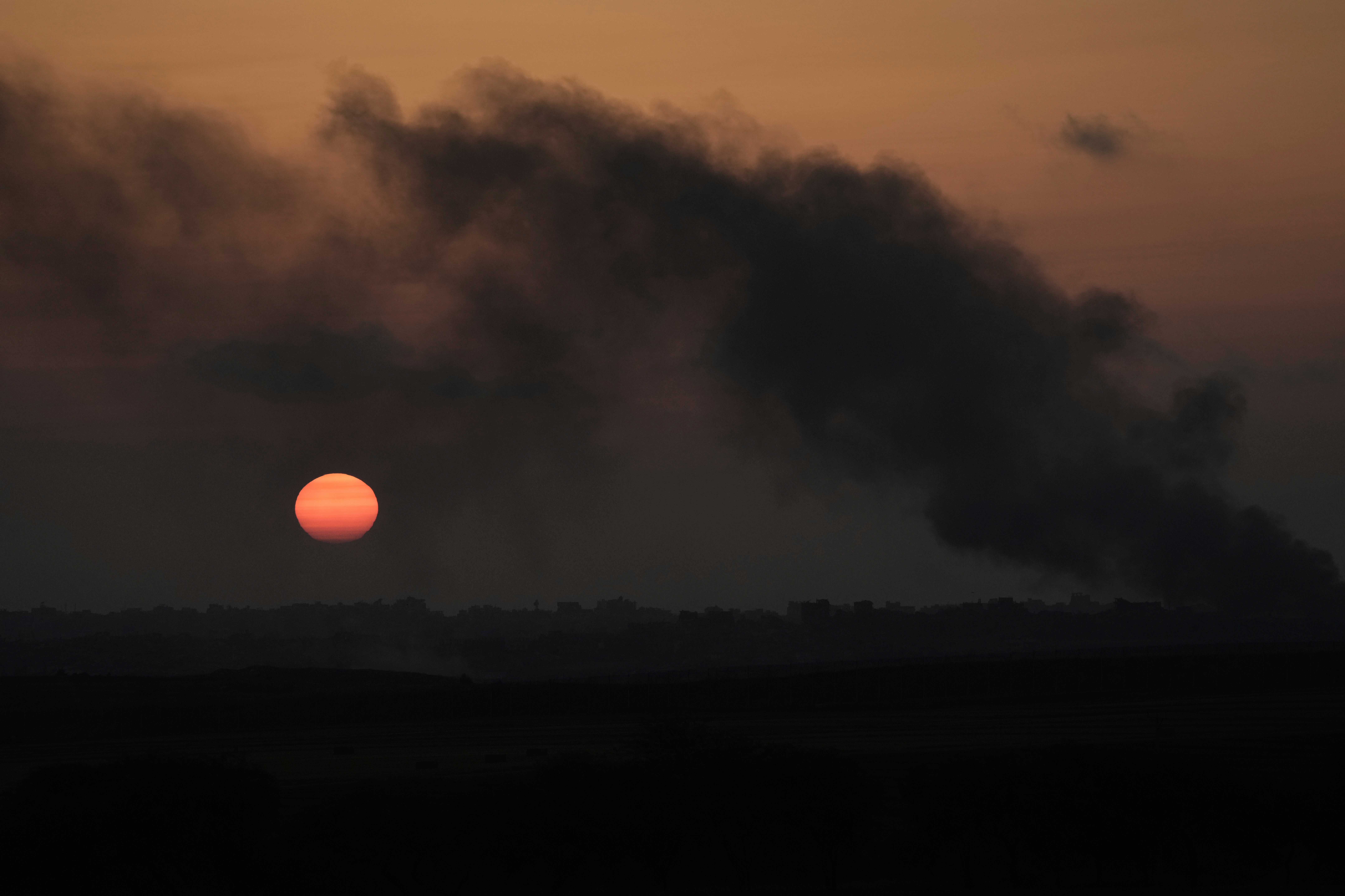 The sun sets as smoke from Israeli bombardment billows over buildings in the northern Gaza Strip, seen from southern Israel, Thursday, June 5, 2025. (AP Photo/Maya Alleruzzo)