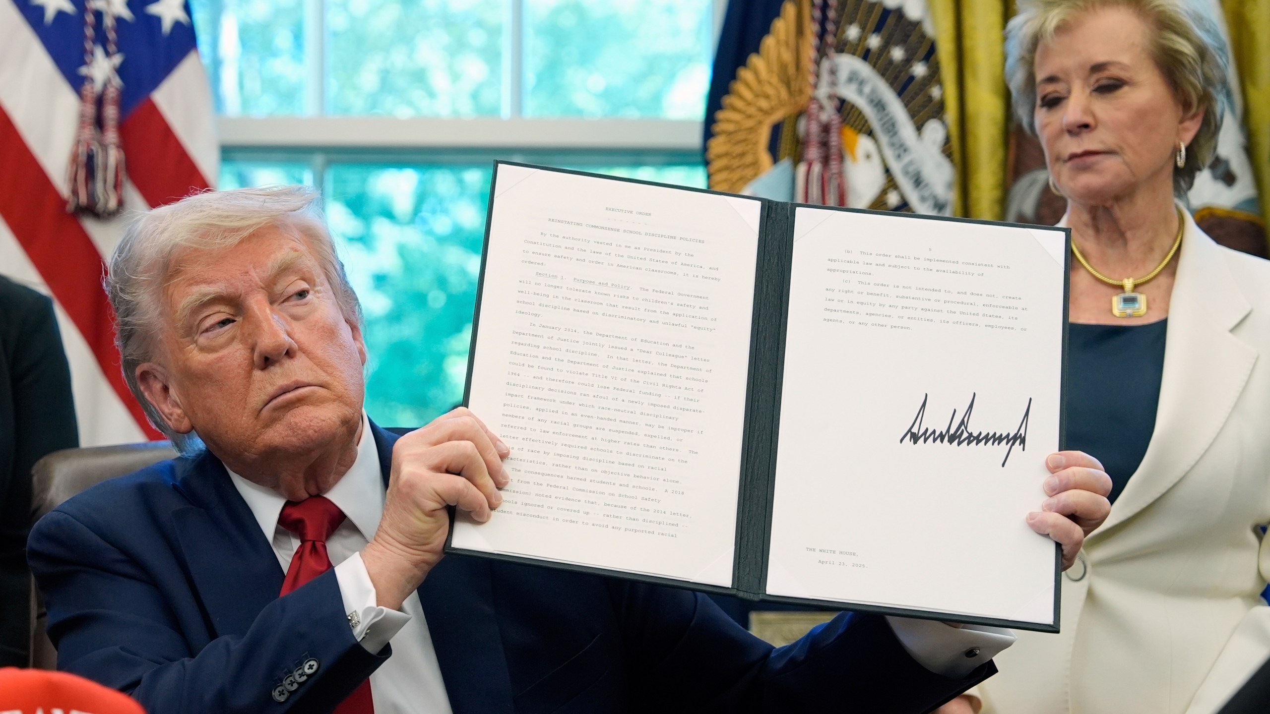 FILE - President Donald Trump holds a signed an executive order relating to school discipline policies as Education Secretary Linda McMahon listens in the Oval Office of the White House, April 23, 2025, in Washington. (AP Photo/Alex Brandon, file)