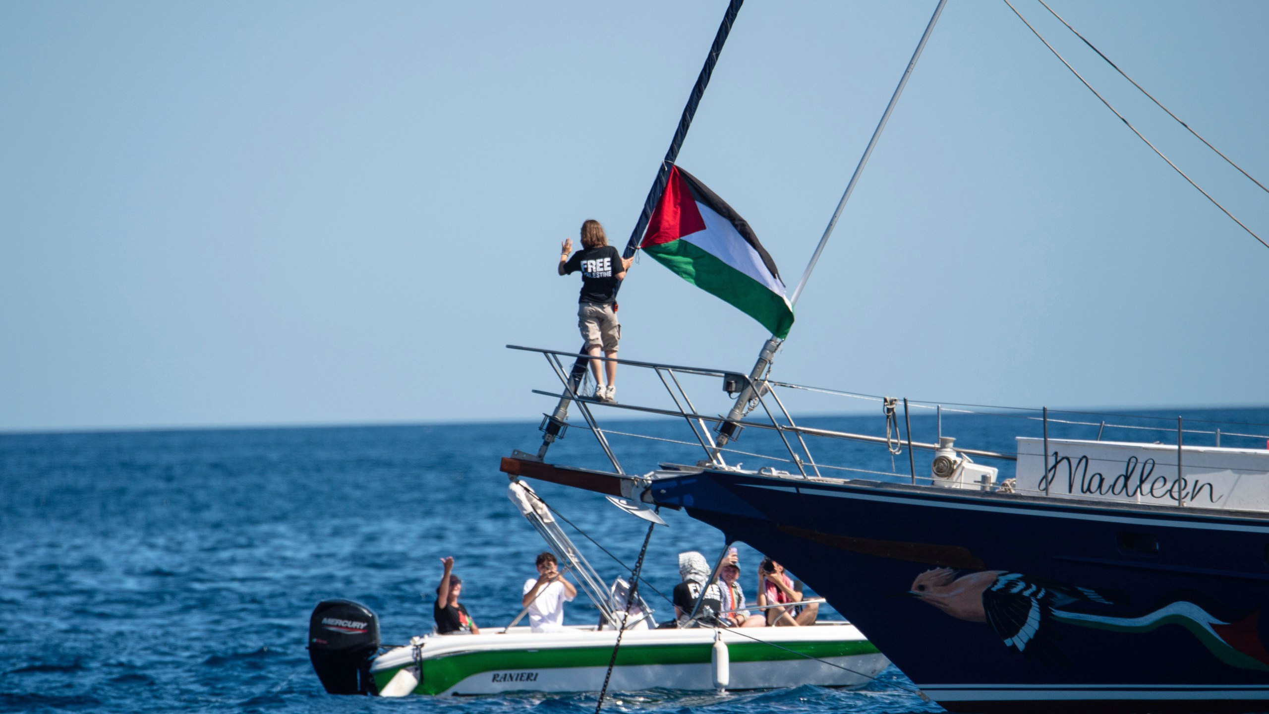 Climate activist Greta Thunberg stands near a Palestinian flag after boarding the Madleen boat and before setting sail for Gaza along with activists of the Freedom Flotilla Coalition, departing from the Sicilian port of Catania, Italy, Sunday, June 1, 2025. (AP Photo/Salvatore Cavalli)