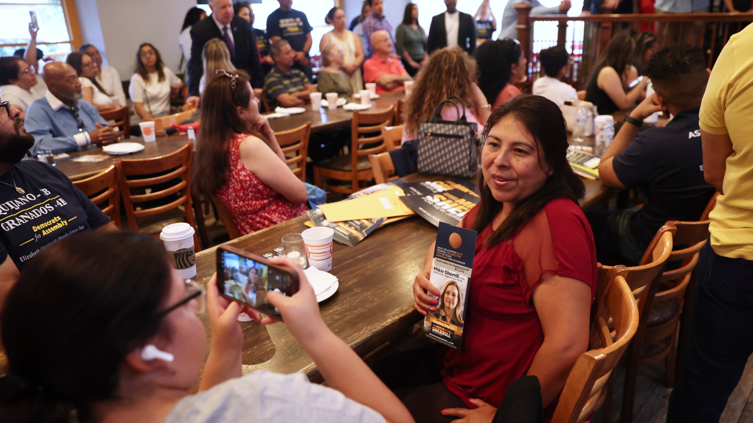 Attendees pose for photos holding a campaign pamphlet of Rep. Mikie Sherrill, D-N.J., during a "Get Out the Vote" rally, Saturday, June 7, 2025, in Elizabeth, N.J. (AP Photo/Heather Khalifa)