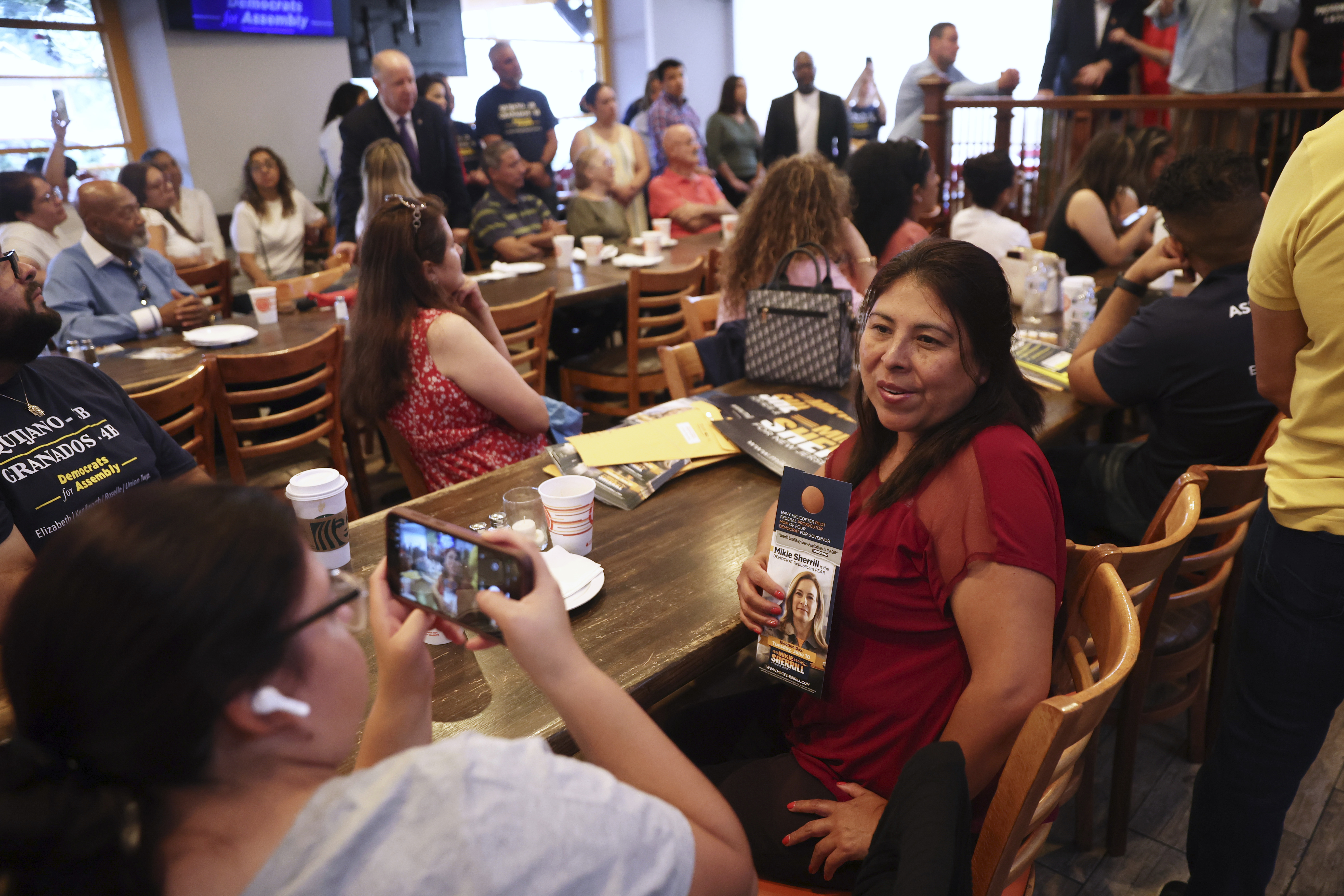 Attendees pose for photos holding a campaign pamphlet of Rep. Mikie Sherrill, D-N.J., during a "Get Out the Vote" rally, Saturday, June 7, 2025, in Elizabeth, N.J. (AP Photo/Heather Khalifa)