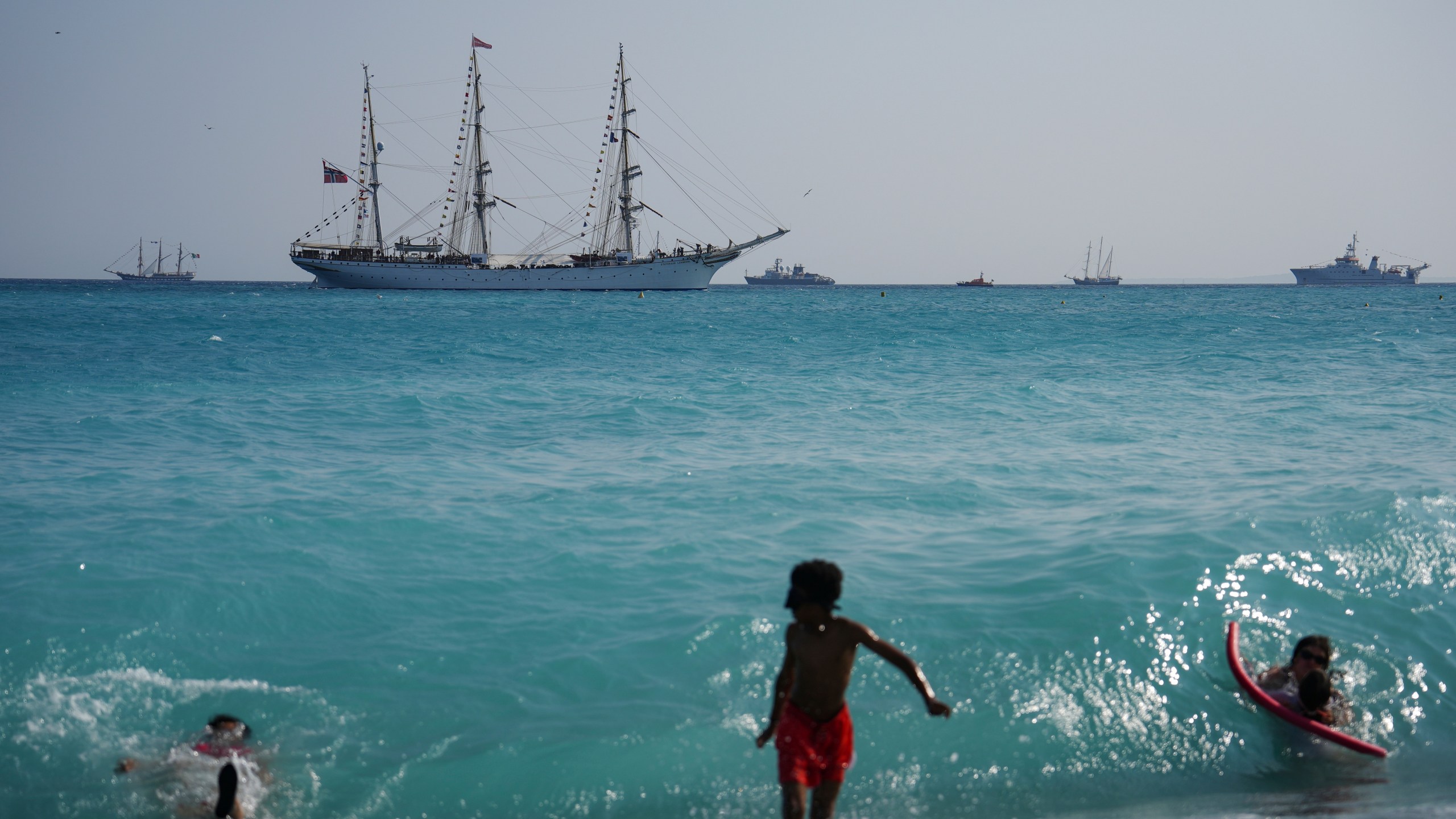 People swim as vessels sail during the "Ocean Wonders" themed event in honor of World Oceans Day ahead of the U.N. Ocean Conference on Sunday, June 8, 2025, in Nice, France. (AP Photo/Annika Hammerschlag)