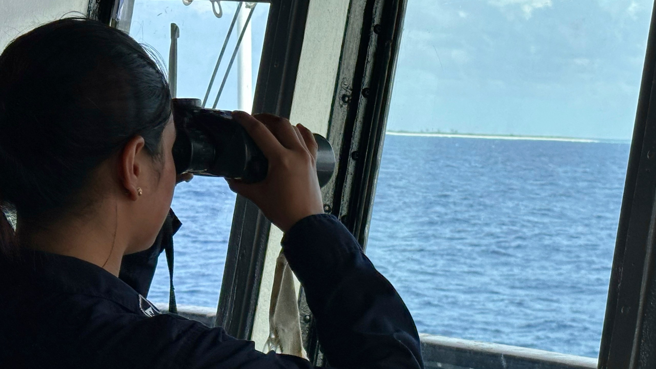 A member of the Philippine Navy uses binoculars as she looks at Northeast Cay, locally known as Parola Island, during a maritime patrol at the disputed South China Sea on Wednesday June 4, 2025. (AP Photo/Joeal Calupitan)