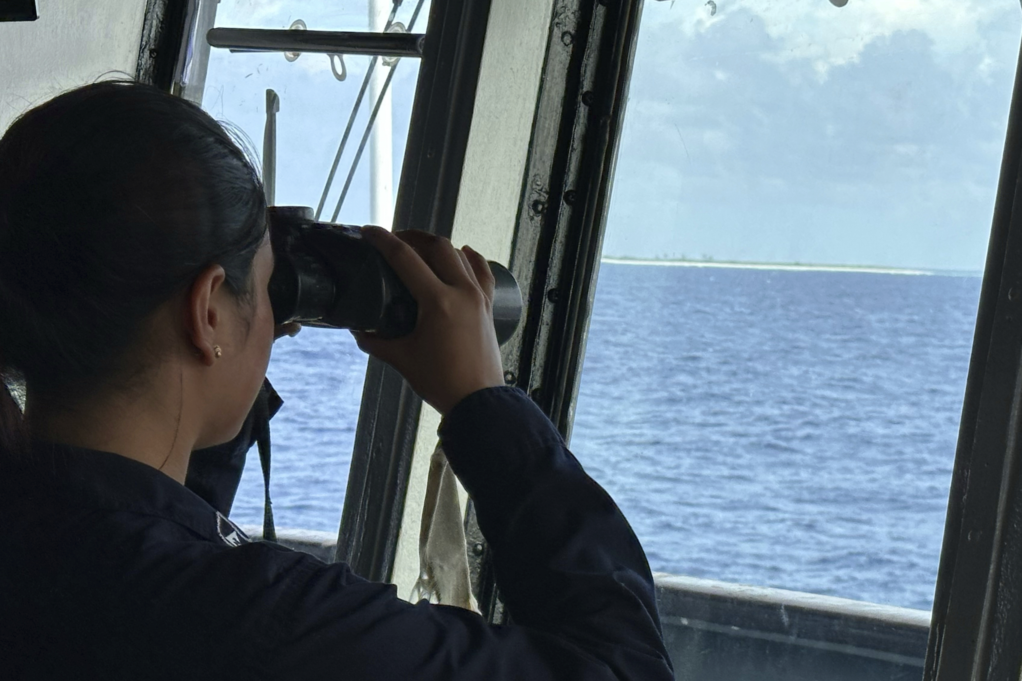 A member of the Philippine Navy uses binoculars as she looks at Northeast Cay, locally known as Parola Island, during a maritime patrol at the disputed South China Sea on Wednesday June 4, 2025. (AP Photo/Joeal Calupitan)