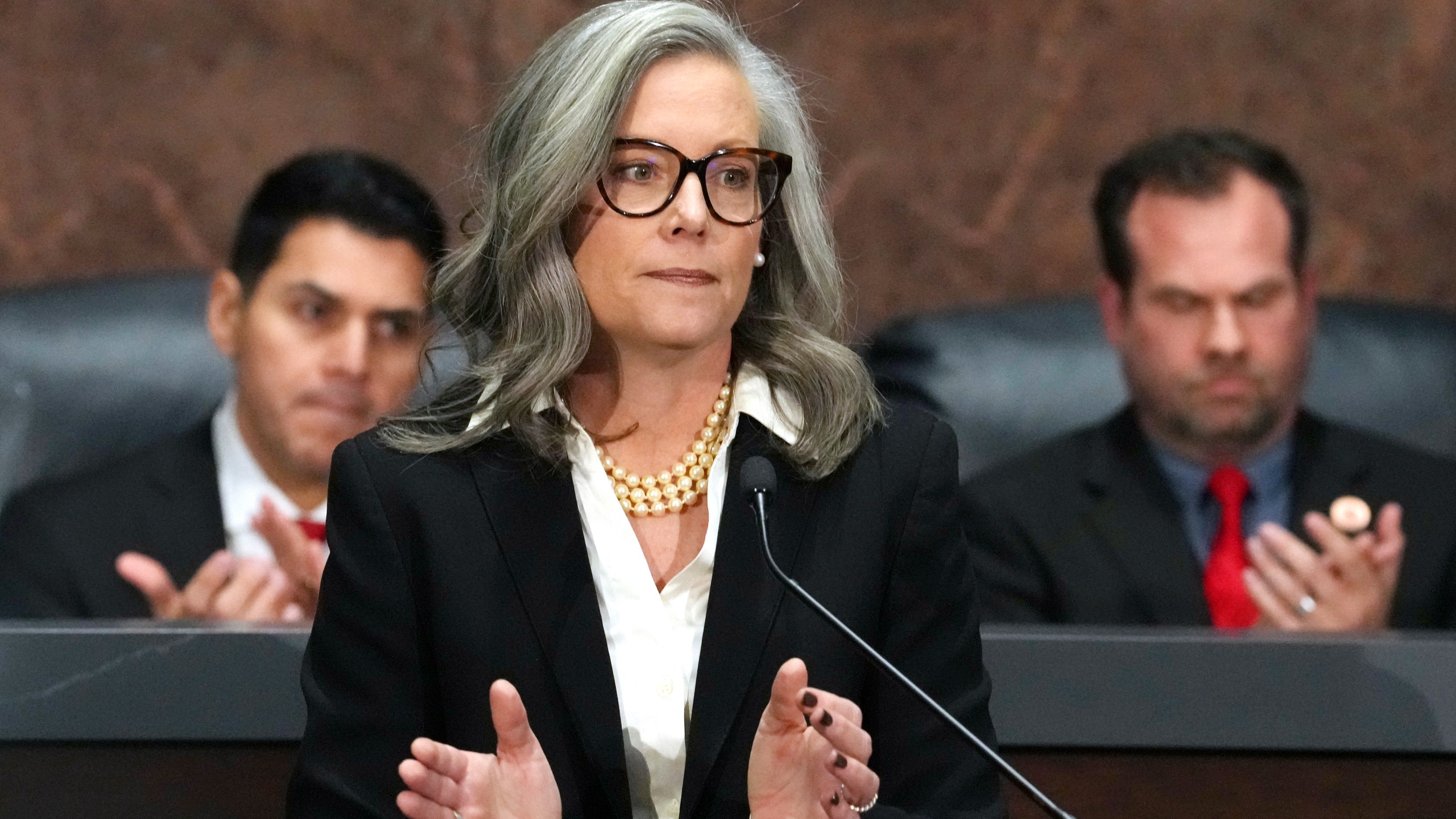 FILE - Arizona Democratic Gov. Katie Hobbs, center, applauds for those affected by the Los Angeles area wildfires as she gives the State of the State address in the House of Representatives at the state Capitol with Speaker of the House Rep. Steve Montenegro, R-Litchfield Park, left, and Senate President Warren Petersen, R-Gilbert, flanking the governor on Jan. 13, 2025, in Phoenix. (AP Photo/Ross D. Franklin, File)