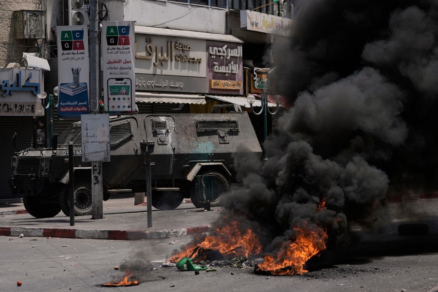 An Israeli armoured vehicle drives near burning tires during a military raid in the West Bank city of Nablus, Tuesday, June 10, 2025. (AP Photo/Majdi Mohammed)