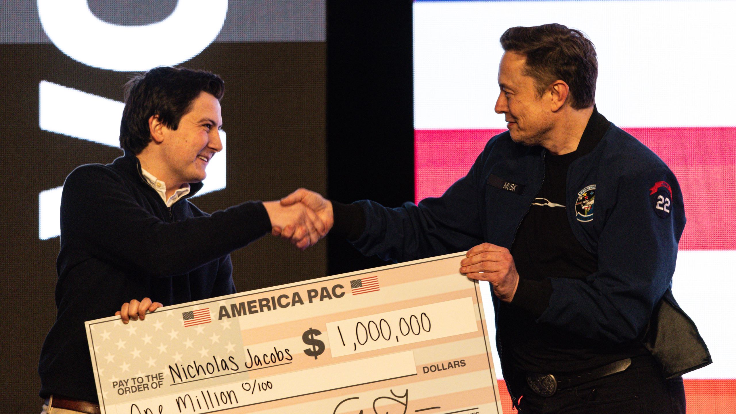 FILE - Elon Musk hands over a million dollar check to Nicholas Jacobs during a town hall in Green Bay, Wis., March 30, 2025. (AP Photo/Jeffrey Phelps, File)