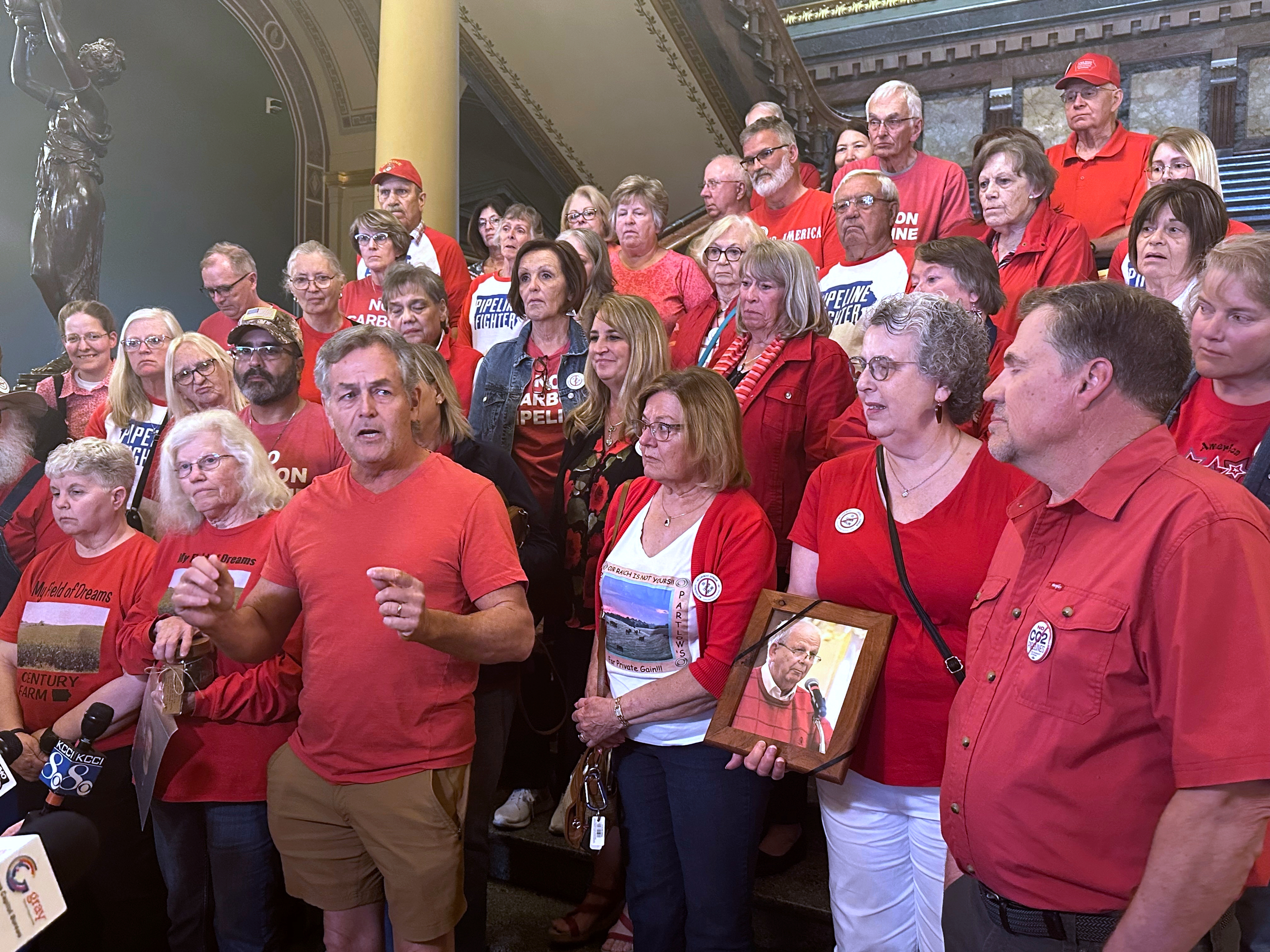 Iowans in red shirts speak to reporters at the statehouse in Des Moines, Iowa, Friday, May 9, 2025 to reiterate their opposition to a massive carbon-capture pipeline project routed across several Midwest states. (AP Photo/Hannah Fingerhut)