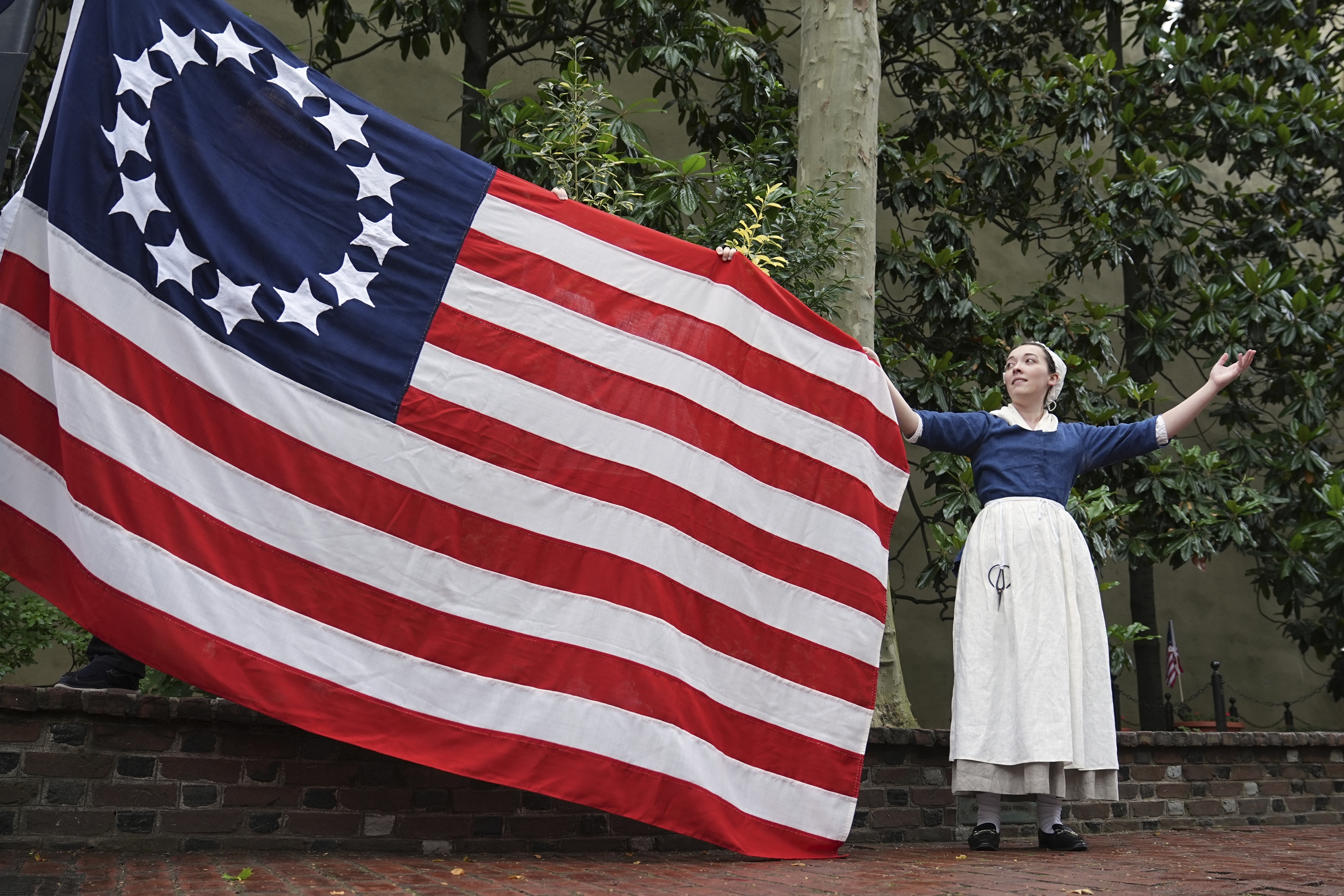 Madeline Burk, portraying Betsy Ross, holds a flag as it is hoisted up at the Betsy Ross House in Philadelphia, Monday, June 9, 2025. (AP Photo/Matt Rourke)