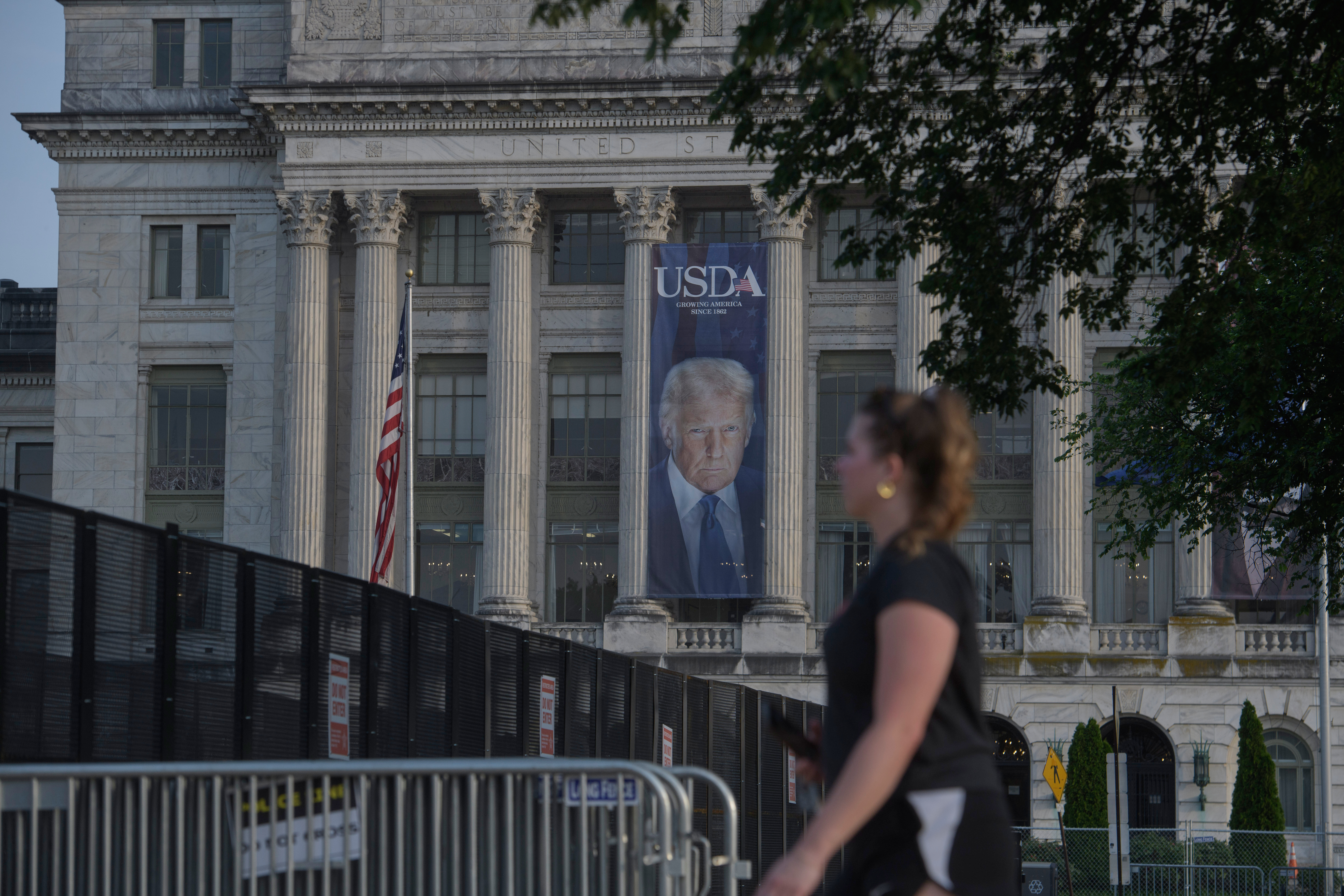 A woman walks past security fencing set up on the National Mall, during preparations for an upcoming military parade commemorating the Army's 250th anniversary and coinciding with President Donald Trump's 79th birthday, Thursday, June 12, 2025, in Washington. (AP Photo/Rod Lamkey, Jr.)