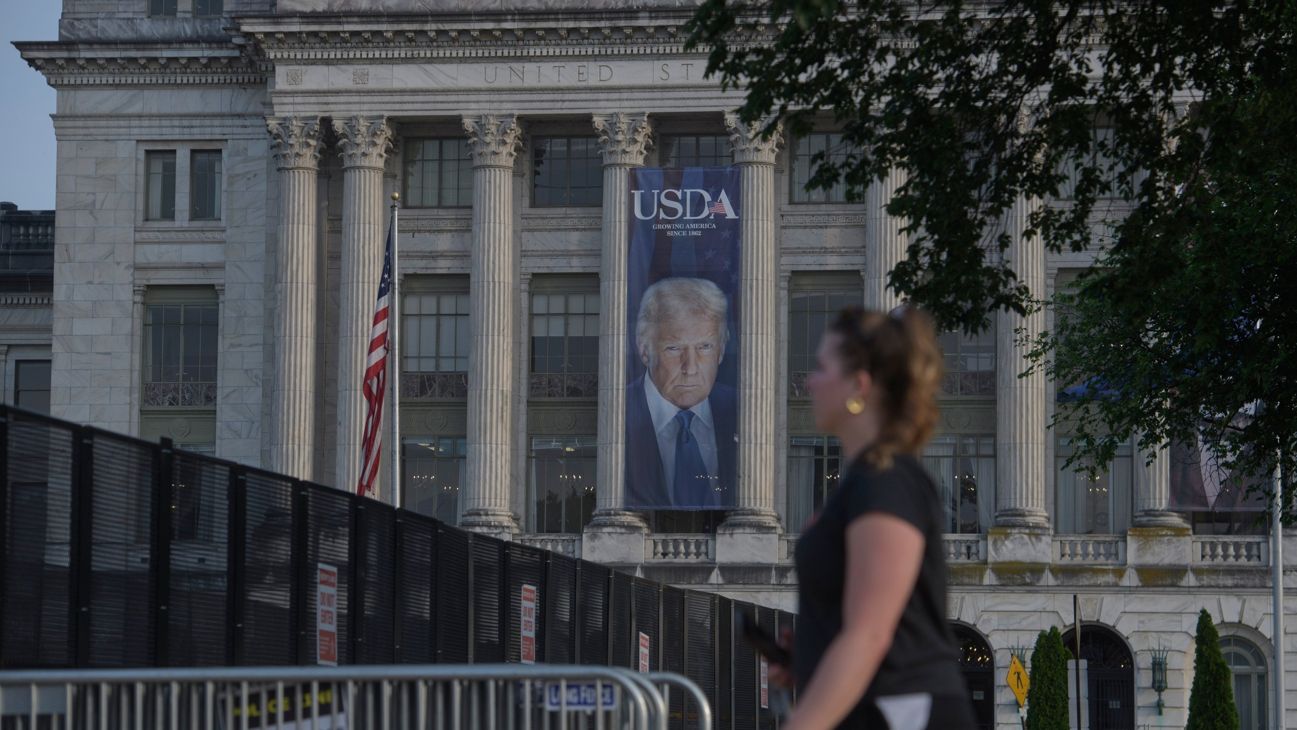 A woman walks past security fencing set up on the National Mall, during preparations for an upcoming military parade commemorating the Army's 250th anniversary and coinciding with President Donald Trump's 79th birthday, Thursday, June 12, 2025, in Washington. (AP Photo/Rod Lamkey, Jr.)