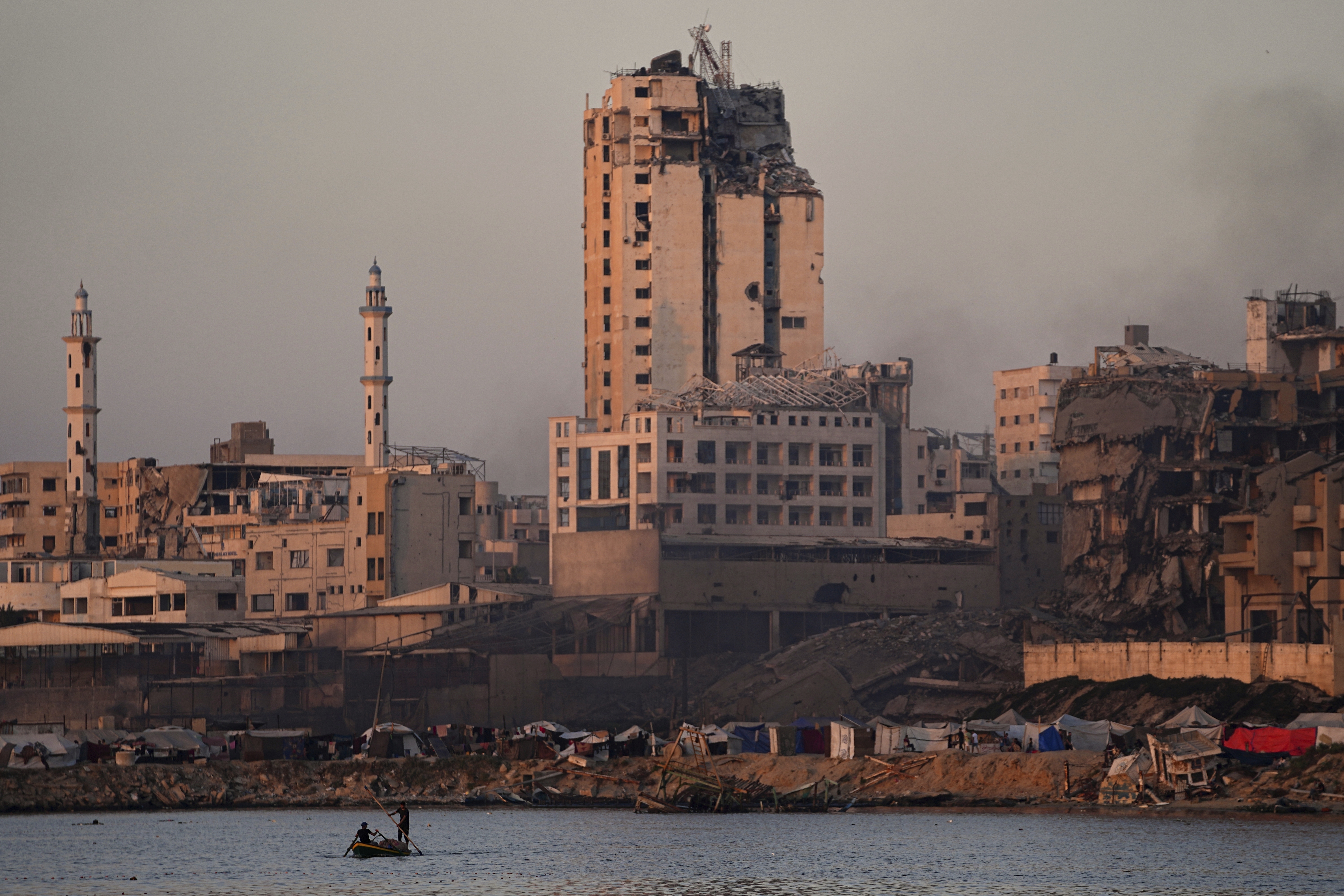 Two Palestinians ride a small boat at the seafront next to a tent camp in the Gaza City port, Friday, June 13, 2025. (AP Photo/Jehad Alshrafi)