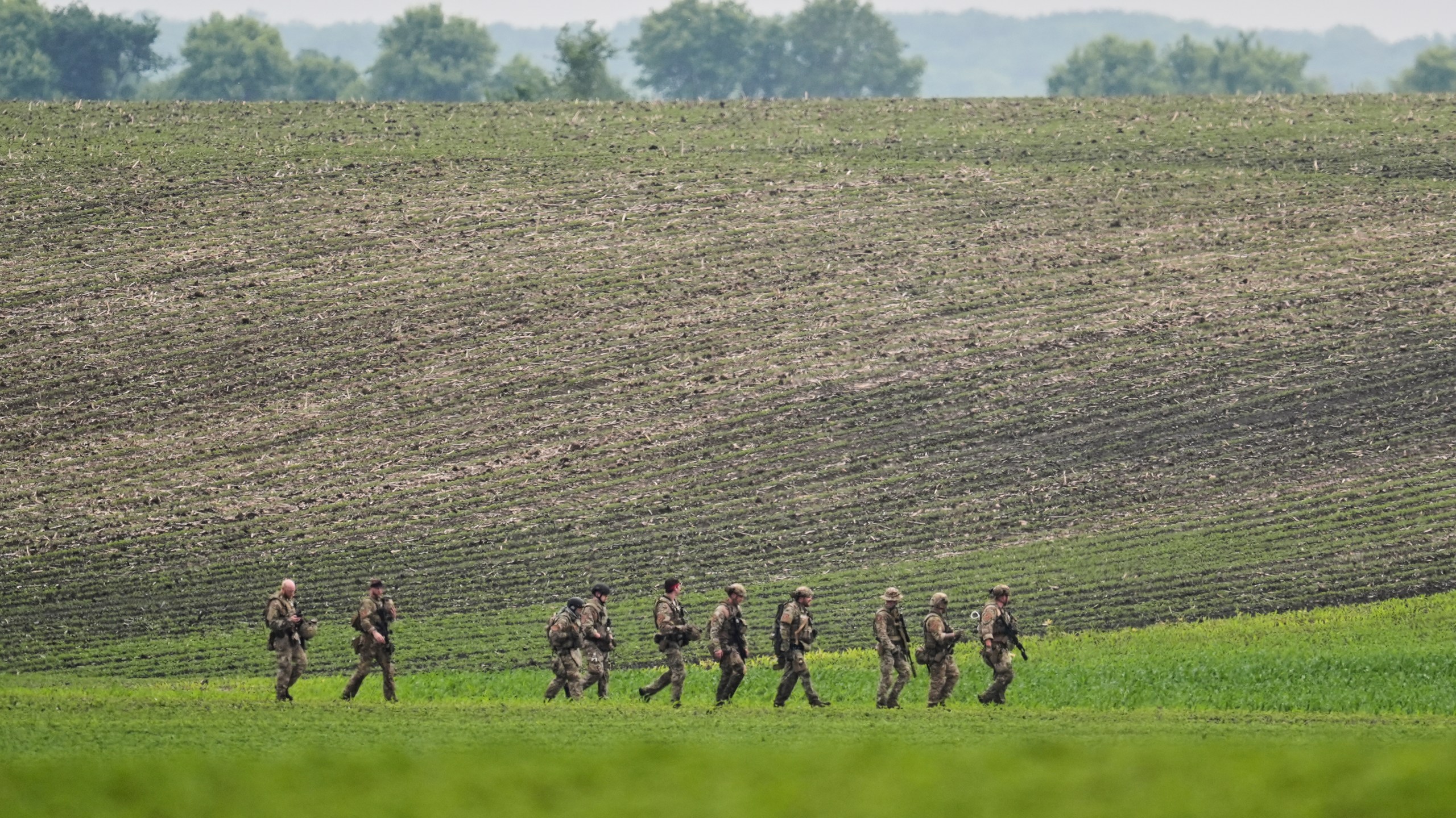 Members of law enforcement agencies walk through a field near a vehicle suspected to belong to shooting suspect, Vance Boelter, Sunday, June 15, 2025, in Belle Plaine, Minn. (AP Photo/George Walker IV)