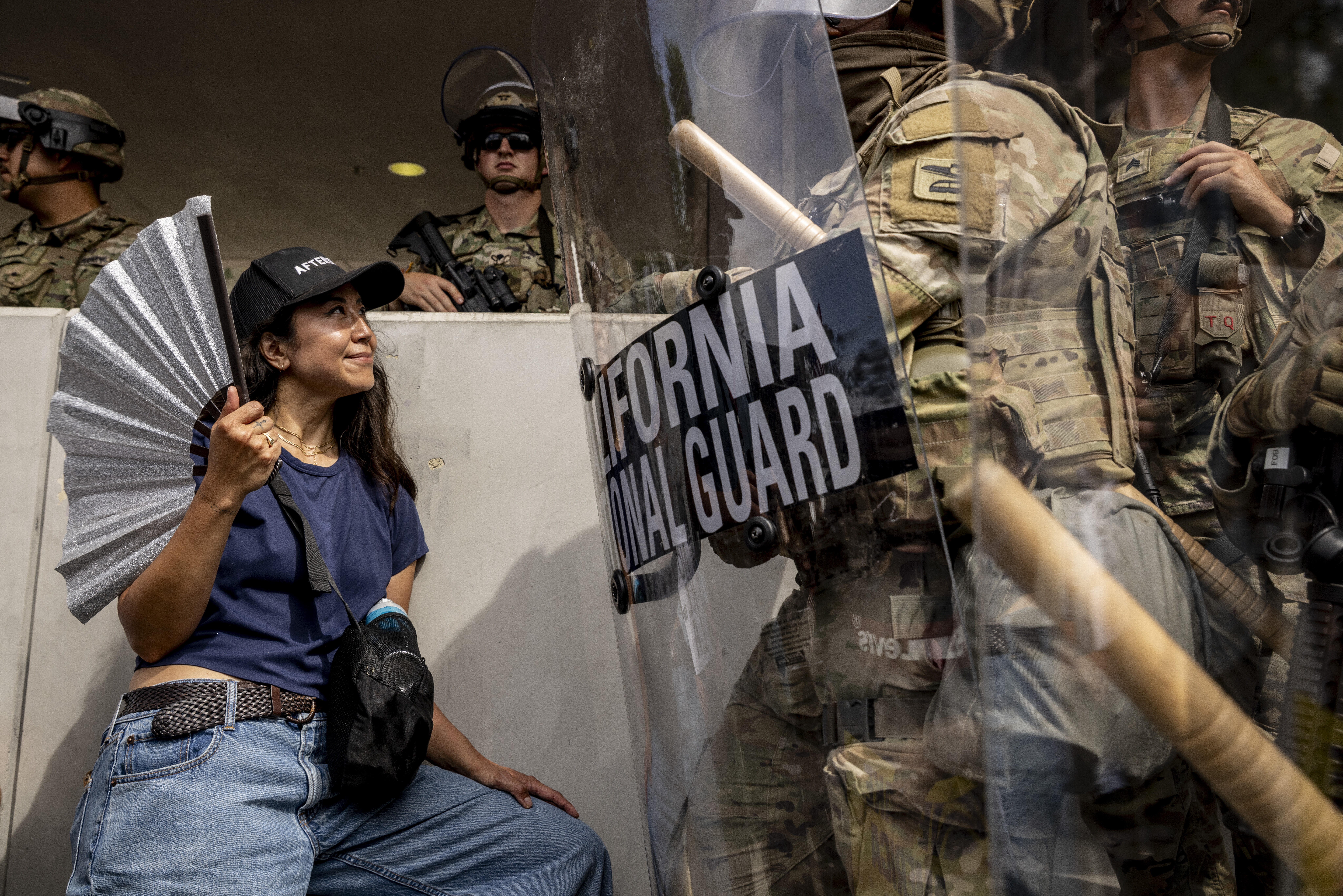 A protester waves a folding fan while standing in front of a California National Guard outside the North Los Angeles Federal Building during a "No Kings" protest in response to a series of United States Immigration and Customs Enforcement (ICE) raids, in Los Angeles, Calif., Saturday, June 14, 2025. (Stephen Lam/San Francisco Chronicle via AP)