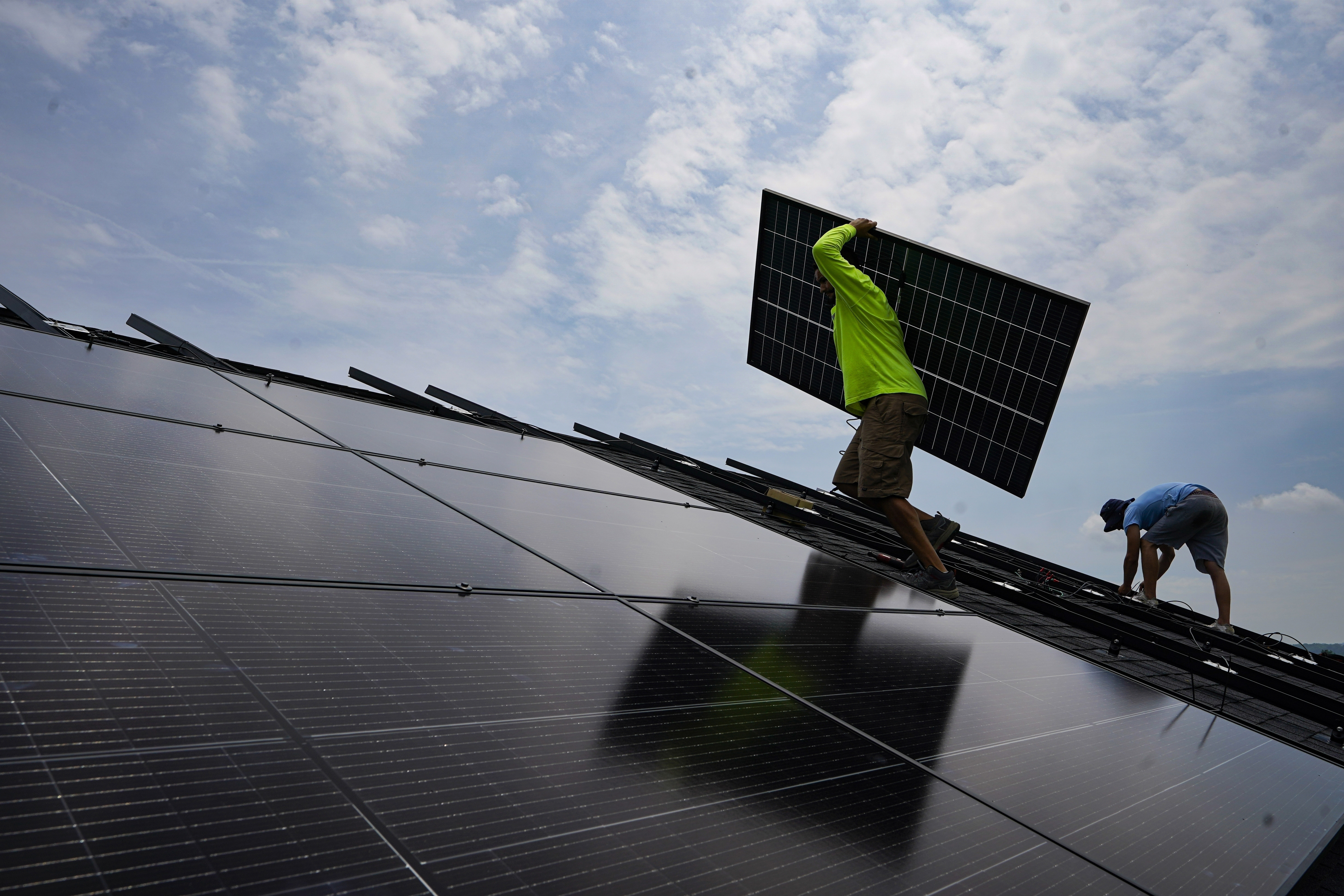 FILE - Nicholas Hartnett, owner of Pure Power Solar, carries a panel as he and Brian Hoeppner, right, install a solar array on the roof of a home in Frankfort, Ky., July 17, 2023. (AP Photo/Michael Conroy, File)