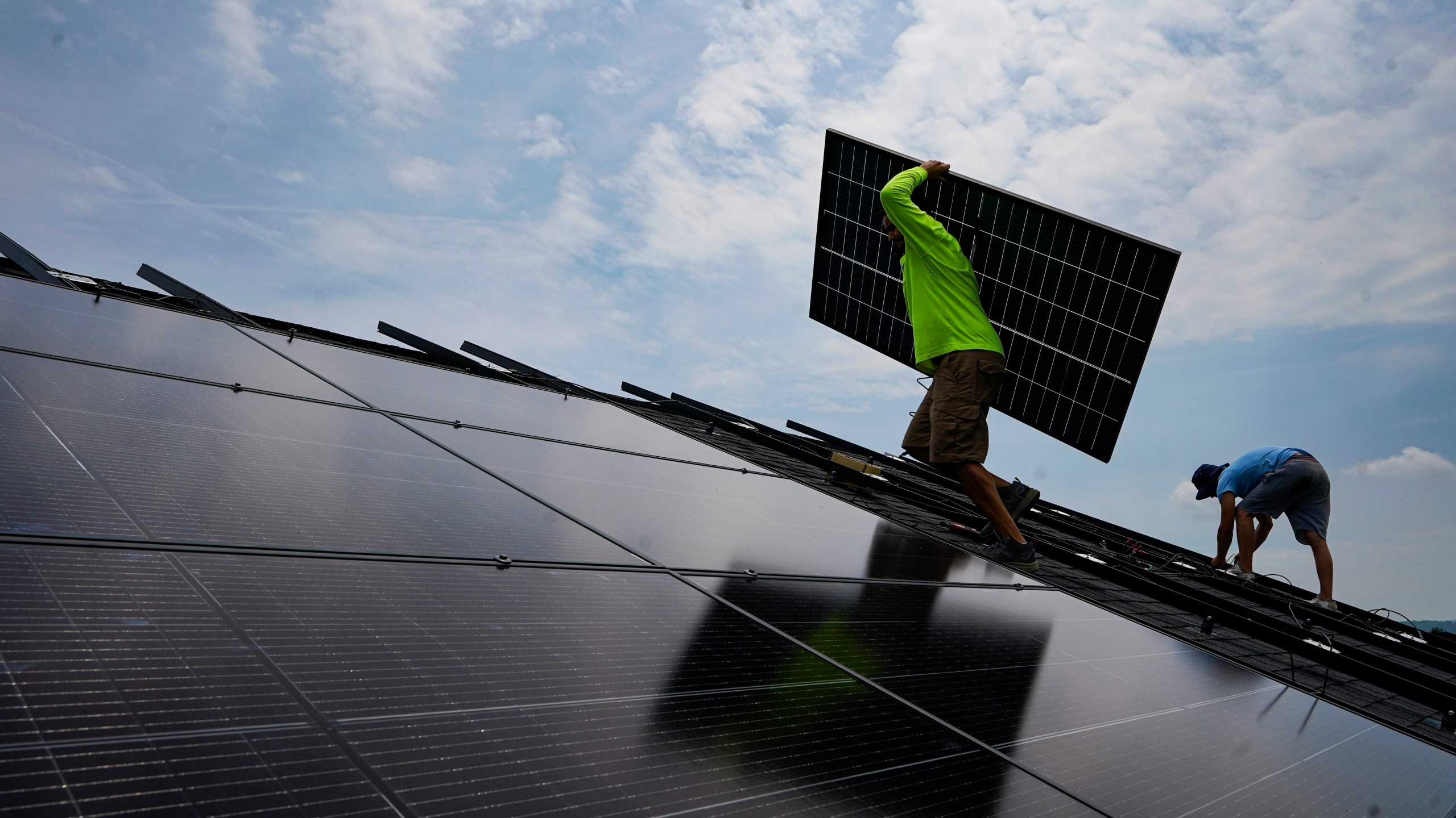 FILE - Nicholas Hartnett, owner of Pure Power Solar, carries a panel as he and Brian Hoeppner, right, install a solar array on the roof of a home in Frankfort, Ky., July 17, 2023. (AP Photo/Michael Conroy, File)