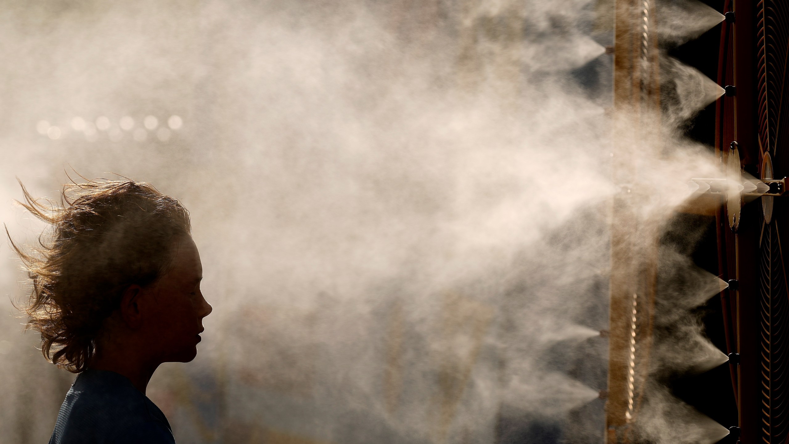 FILE - Michael Mullenax, 10, from Lee's Summit, Mo., cools off in a mister at Kauffman Stadium before a baseball game between the Kansas City Royals and the Miami Marlins, June 24, 2024, in Kansas City, Mo. (AP Photo/Charlie Riedel, File)