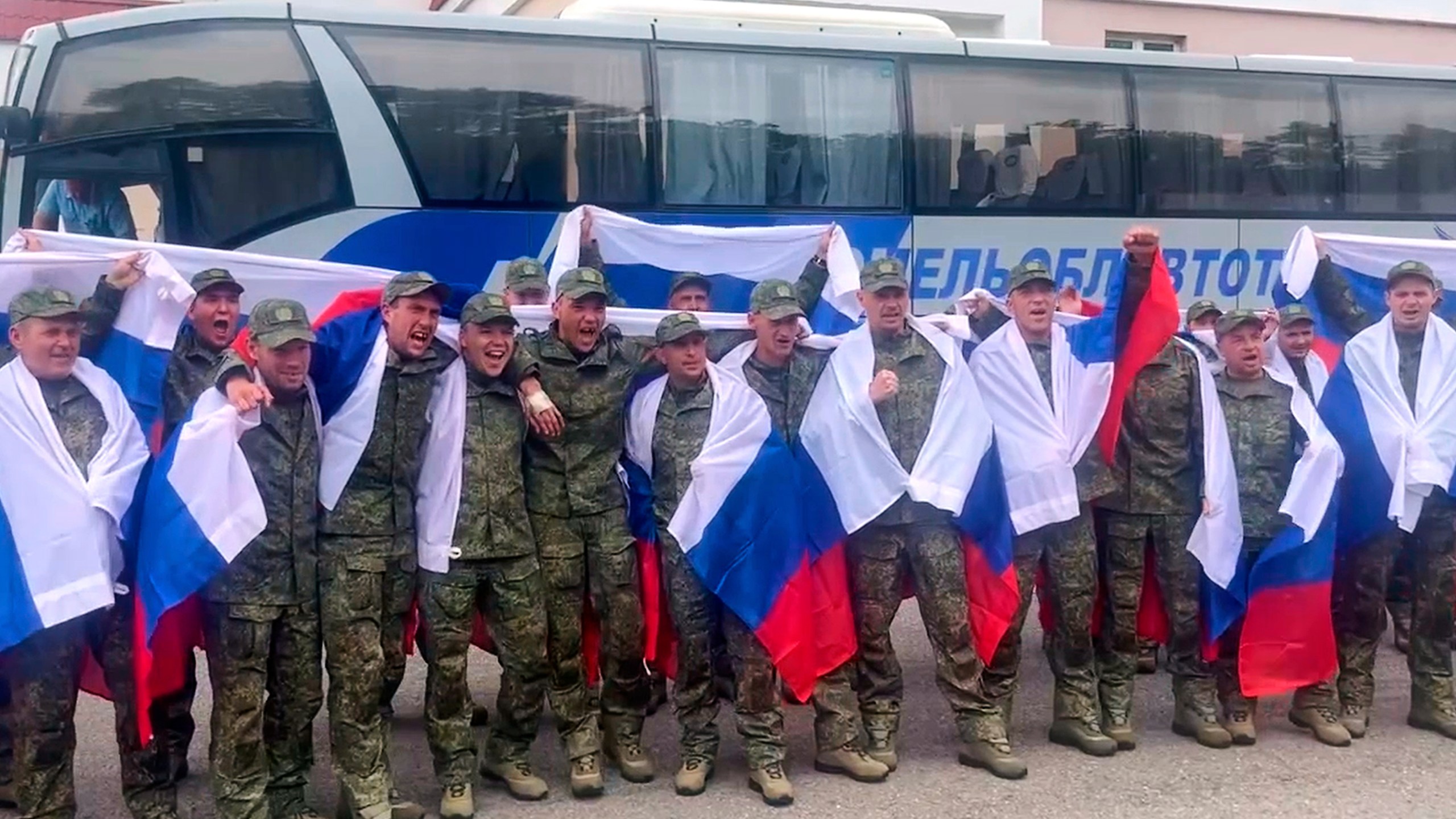 In this photo taken from video distributed by Russian Defense Ministry Press Service on Thursday, June 19, 2025, Russian servicemen with Russian national flags pose for a photo at an exchange area in Belarus after returning from captivity during a POWs exchange of a group of servicemen between Russia and Ukraine. (Russian Defense Ministry Press Service via AP)