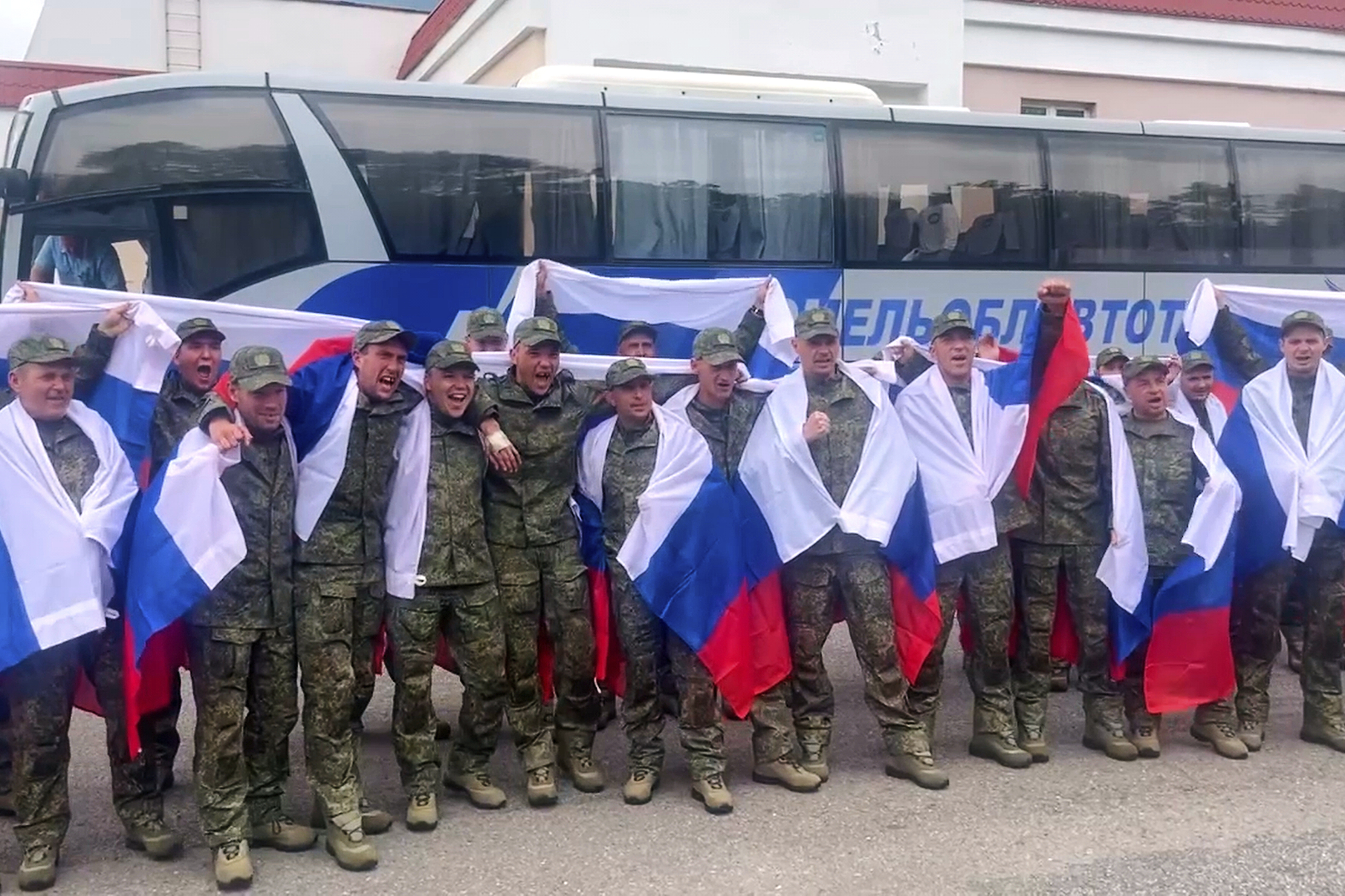 In this photo taken from video distributed by Russian Defense Ministry Press Service on Thursday, June 19, 2025, Russian servicemen with Russian national flags pose for a photo at an exchange area in Belarus after returning from captivity during a POWs exchange of a group of servicemen between Russia and Ukraine. (Russian Defense Ministry Press Service via AP)