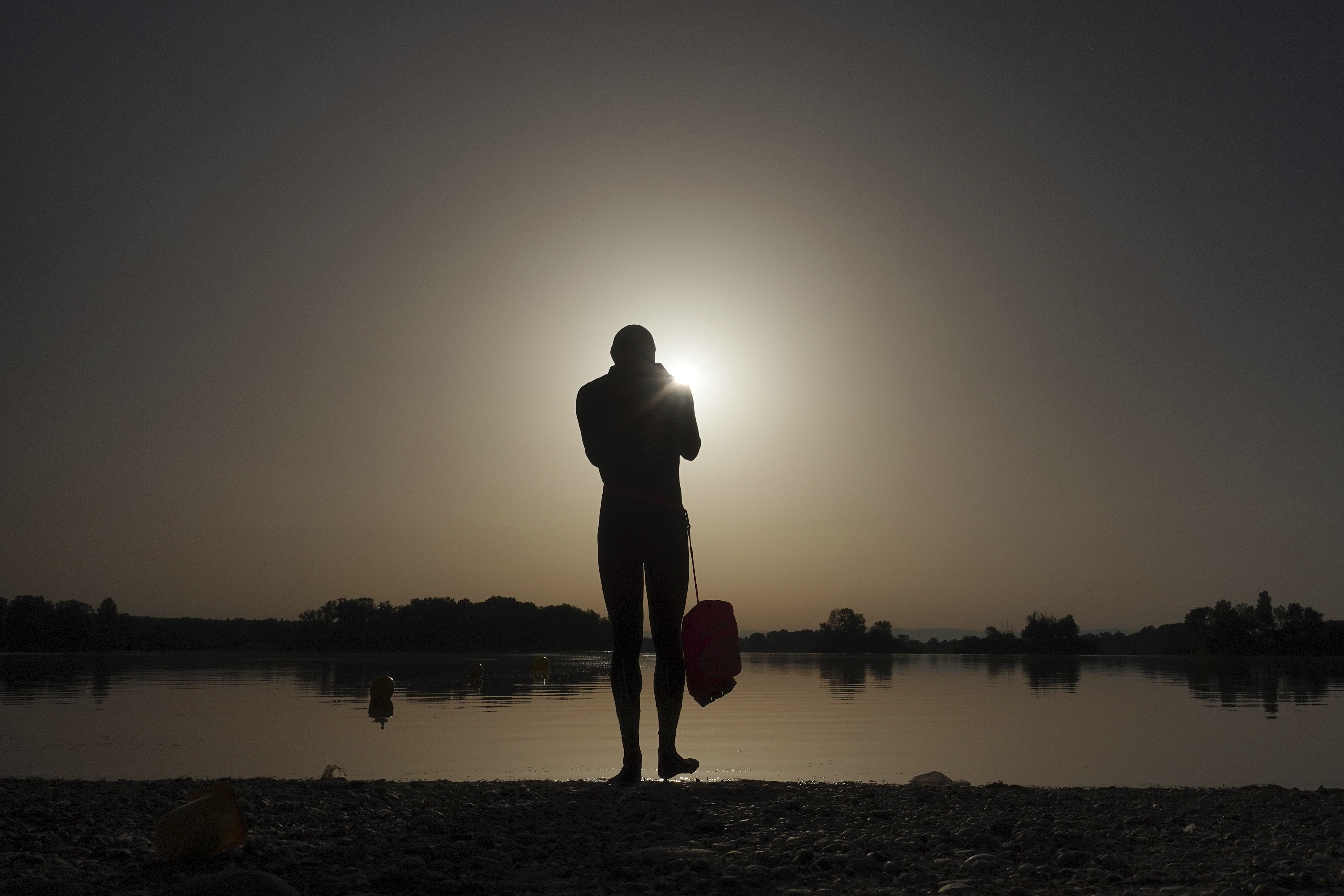 FILE - A man prepares to enter the water as the sun rises above the Miribel lake, outside Lyon, France, June 18, 2022. (AP Photo/Laurent Cipriani, File)