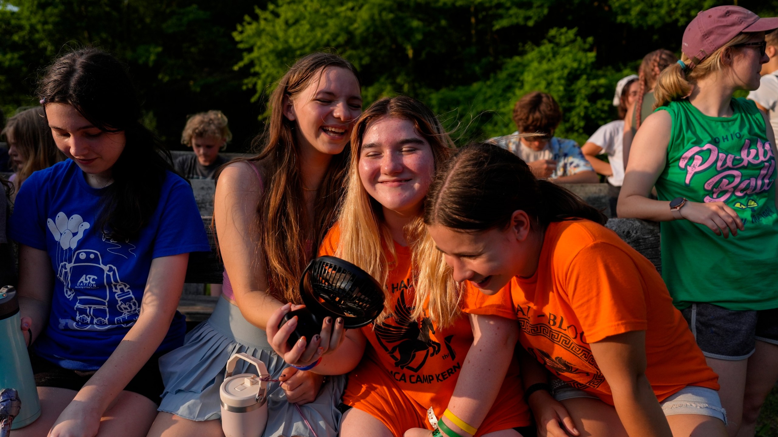 FILE - Mirabelle Demske, second from left, uses a portable electric fan to cool off her friends Faith Hamzy, center, and Annie Sayre, second from right, June 20, 2024, at YMCA Camp Kern in Oregonia, Ohio. (AP Photo/Joshua A. Bickel, File)