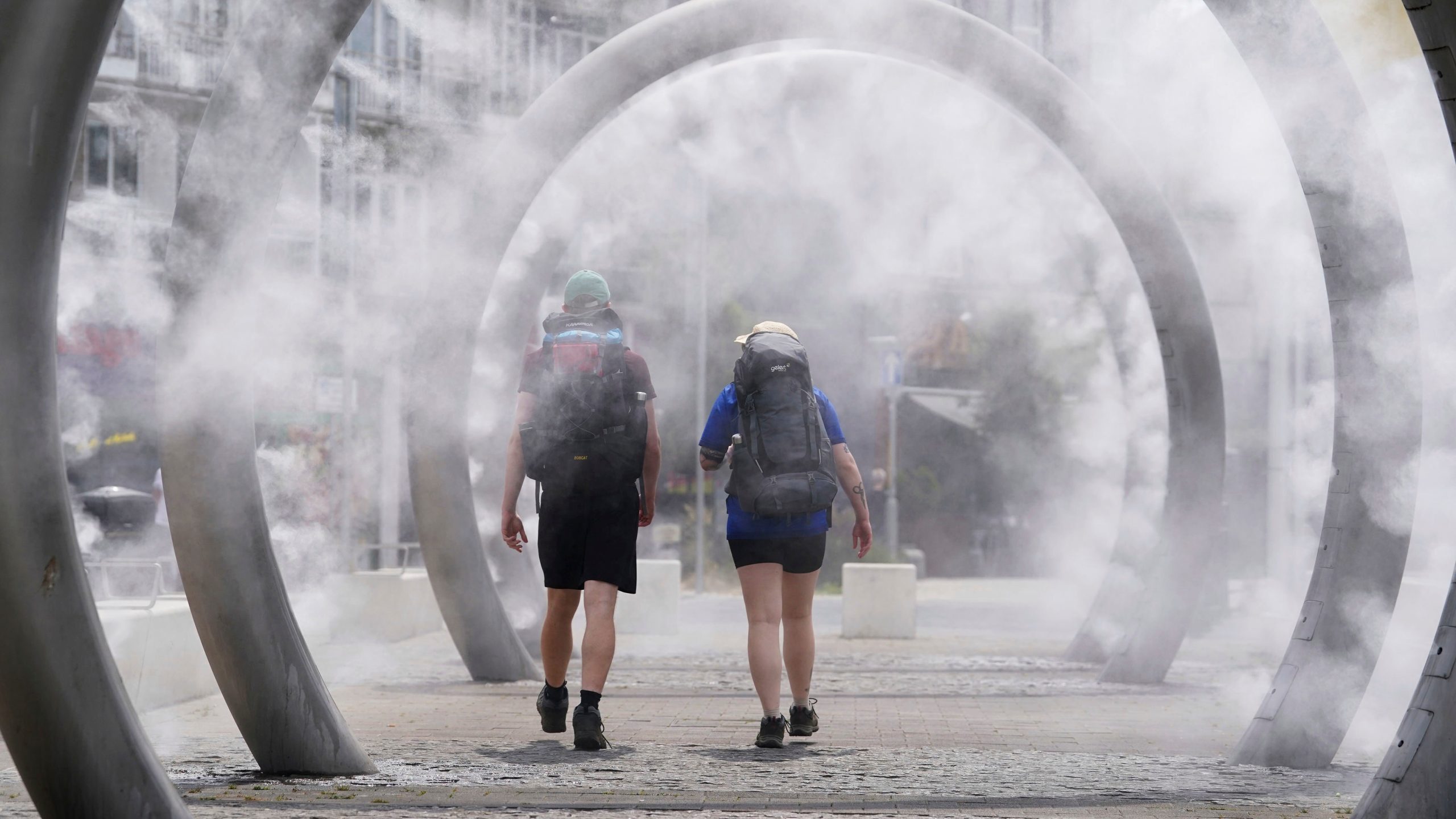 Walkers cool off as they walk through a water feature spraying a fine mist in Dover, England, Friday, June 20, 2025. (Gareth Fuller/PA via AP)