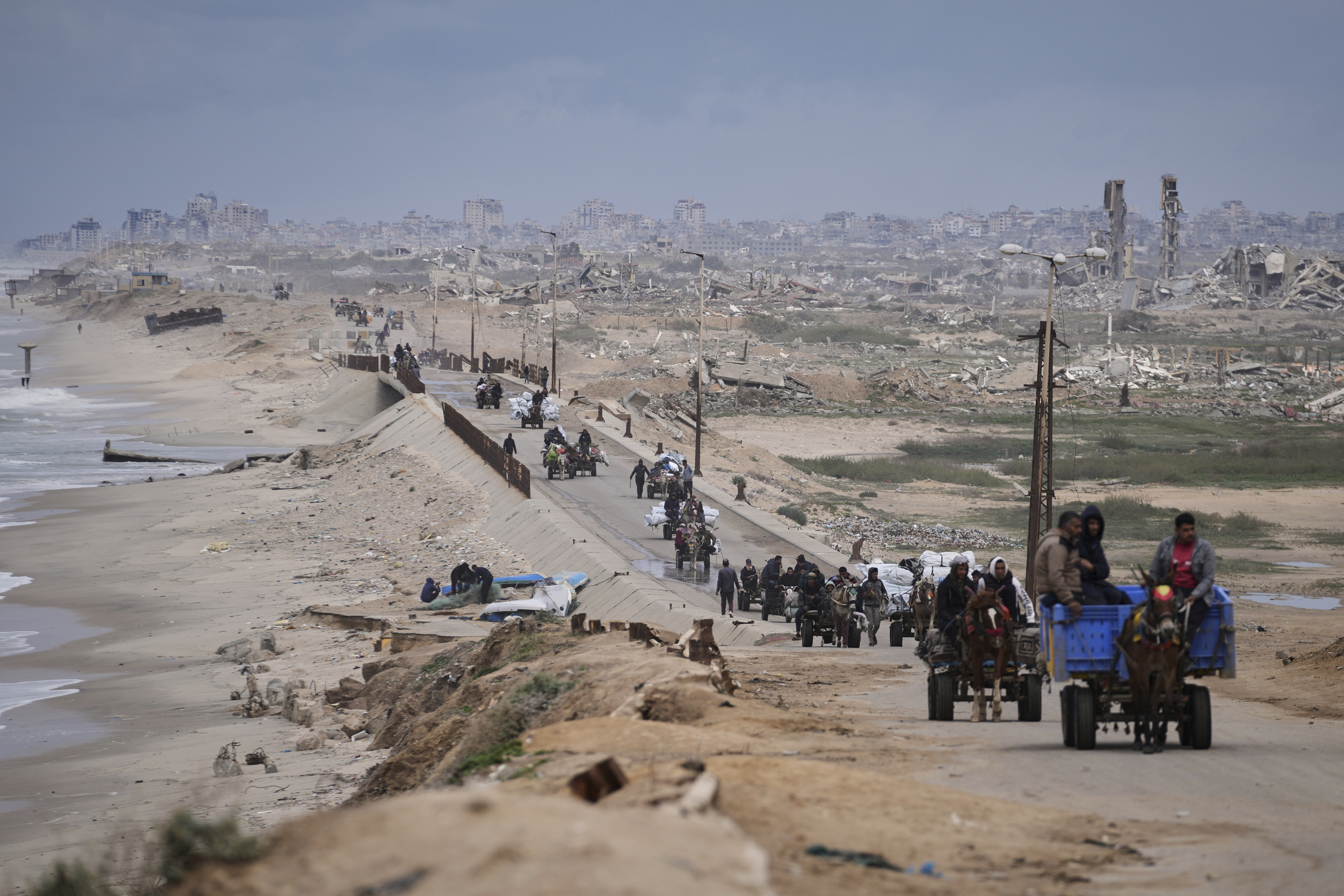 FILE - Displaced Palestinians, carrying their belongings move between southern and northern Gaza along a beach road, in the outskirts of Gaza City, on March 21, 2025. (AP Photo/Abdel Kareem Hana, File)
