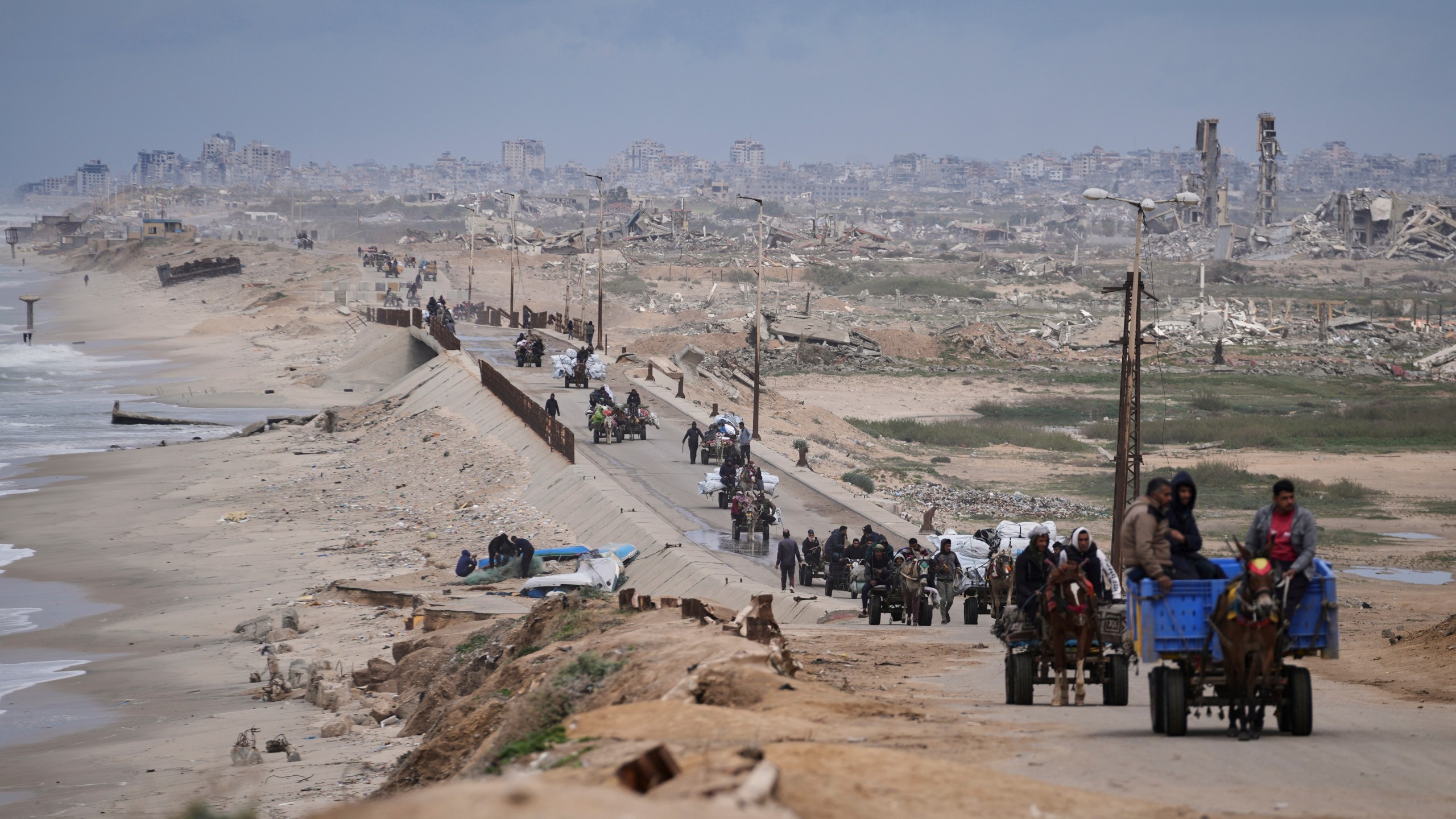 FILE - Displaced Palestinians, carrying their belongings move between southern and northern Gaza along a beach road, in the outskirts of Gaza City, on March 21, 2025. (AP Photo/Abdel Kareem Hana, File)