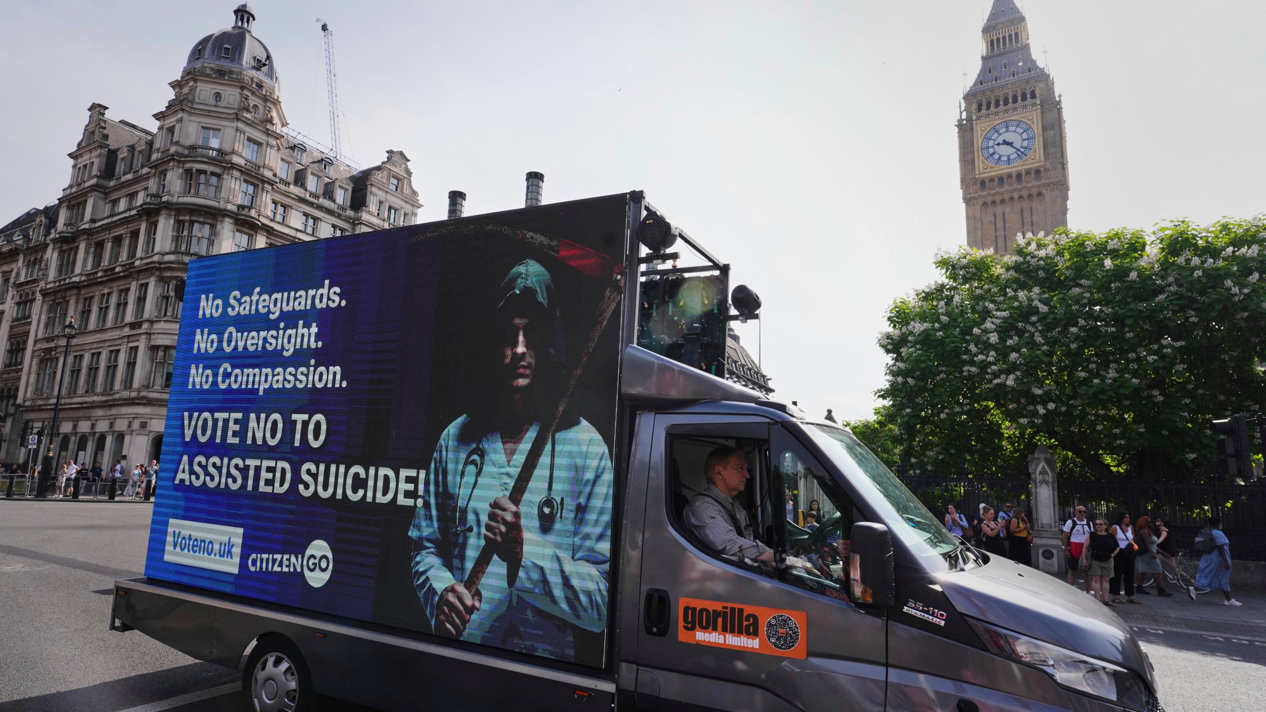 A van displaying a sign passes Big Ben as demonstrators both for and against assisted dying hold banners outside Parliament in London, Friday, June 20, 2025, as British lawmakers are set to vote Friday on whether to back a bill to help terminally ill adults end their lives in England and Wales. (AP Photo/Kirsty Wigglesworth)