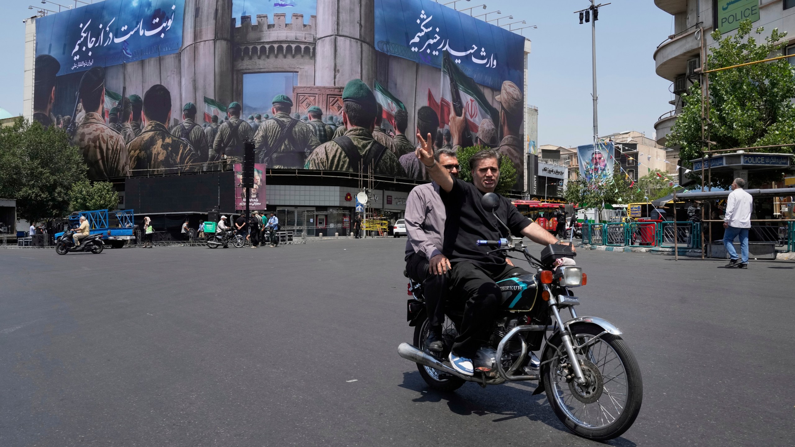 A man flashes a victory sign while riding his motorbike past an anti-Israeli banner depicting Iranian soldiers heading to attack Israeli territory, at Islamic Revolution Square in Tehran, Iran, Saturday, June 14, 2025. (AP Photo/Vahid Salemi)
