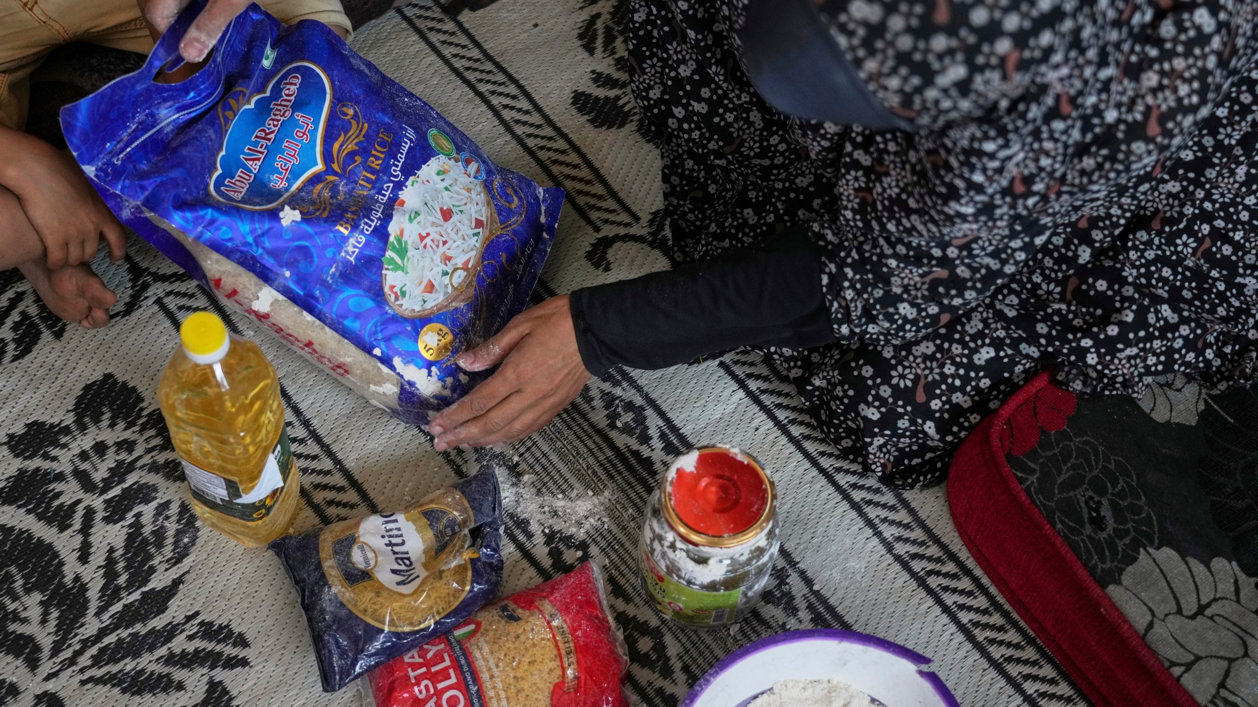 Anwaar Saleh, 32, displays the donated food her husband, Omar al-Hobi, collected at a distribution center run by private contractor the Gaza Humanitarian Foundation in the southern Gaza Strip, after he arrived at their family's tent in Khan Younis, Tuesday, June 10, 2025. (AP Photo/Abdel Kareem Hana)