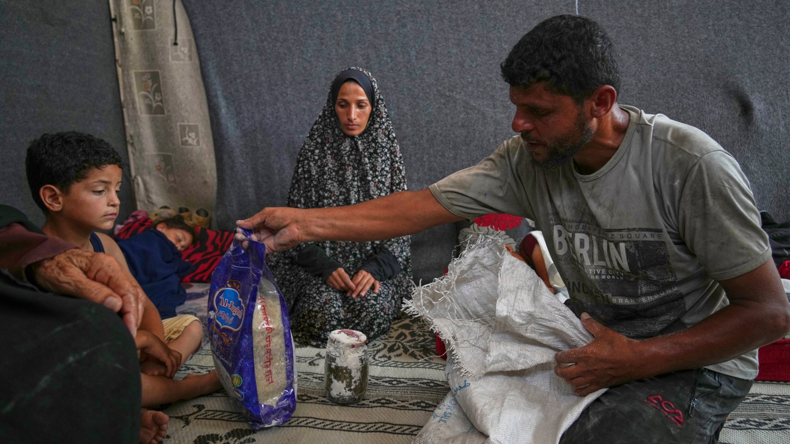 Omar al-Hobi, 43, from Rafah, unpacks a bag of food he collected at a distribution center run by private contractor the Gaza Humanitarian Foundation in the southern Gaza Strip, as he arrives at his family's tent in Khan Younis, Tuesday, June 10, 2025. At left are his children and his wife, Anwaar Saleh.(AP Photo/Abdel Kareem Hana)