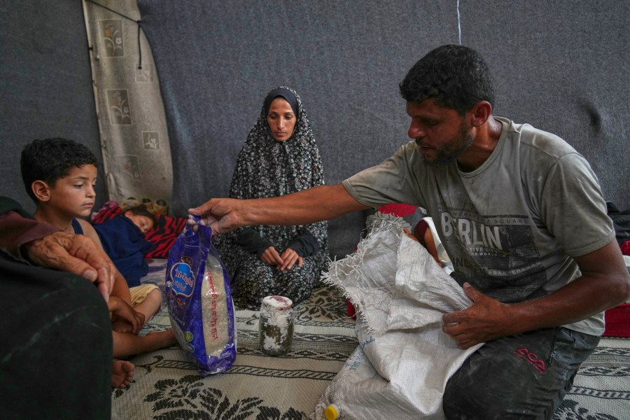 Omar al-Hobi, 43, from Rafah, unpacks a bag of food he collected at a distribution center run by private contractor the Gaza Humanitarian Foundation in the southern Gaza Strip, as he arrives at his family's tent in Khan Younis, Tuesday, June 10, 2025. At left are his children and his wife, Anwaar Saleh.(AP Photo/Abdel Kareem Hana)